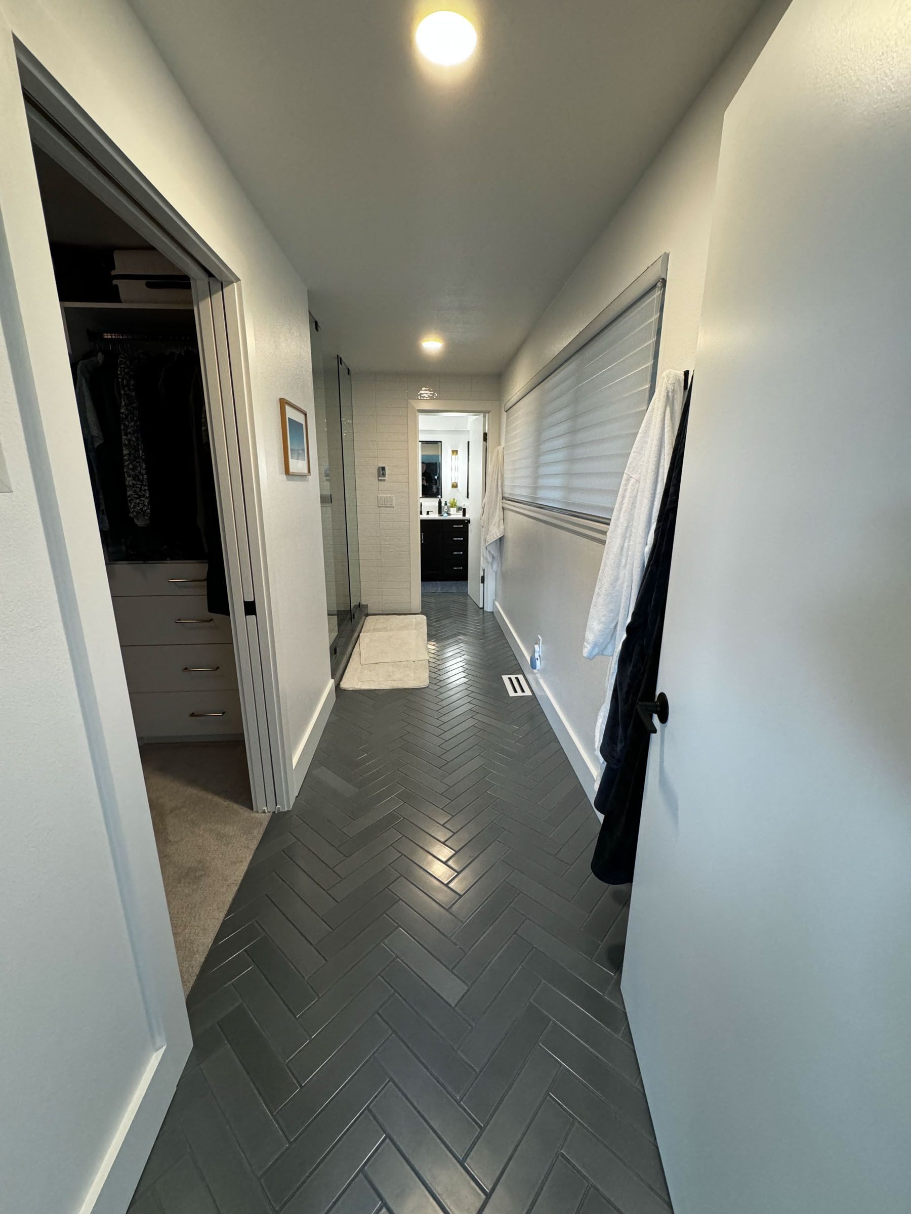 Narrow hallway with gray herringbone tile floor, white walls, and doors on the left and right.