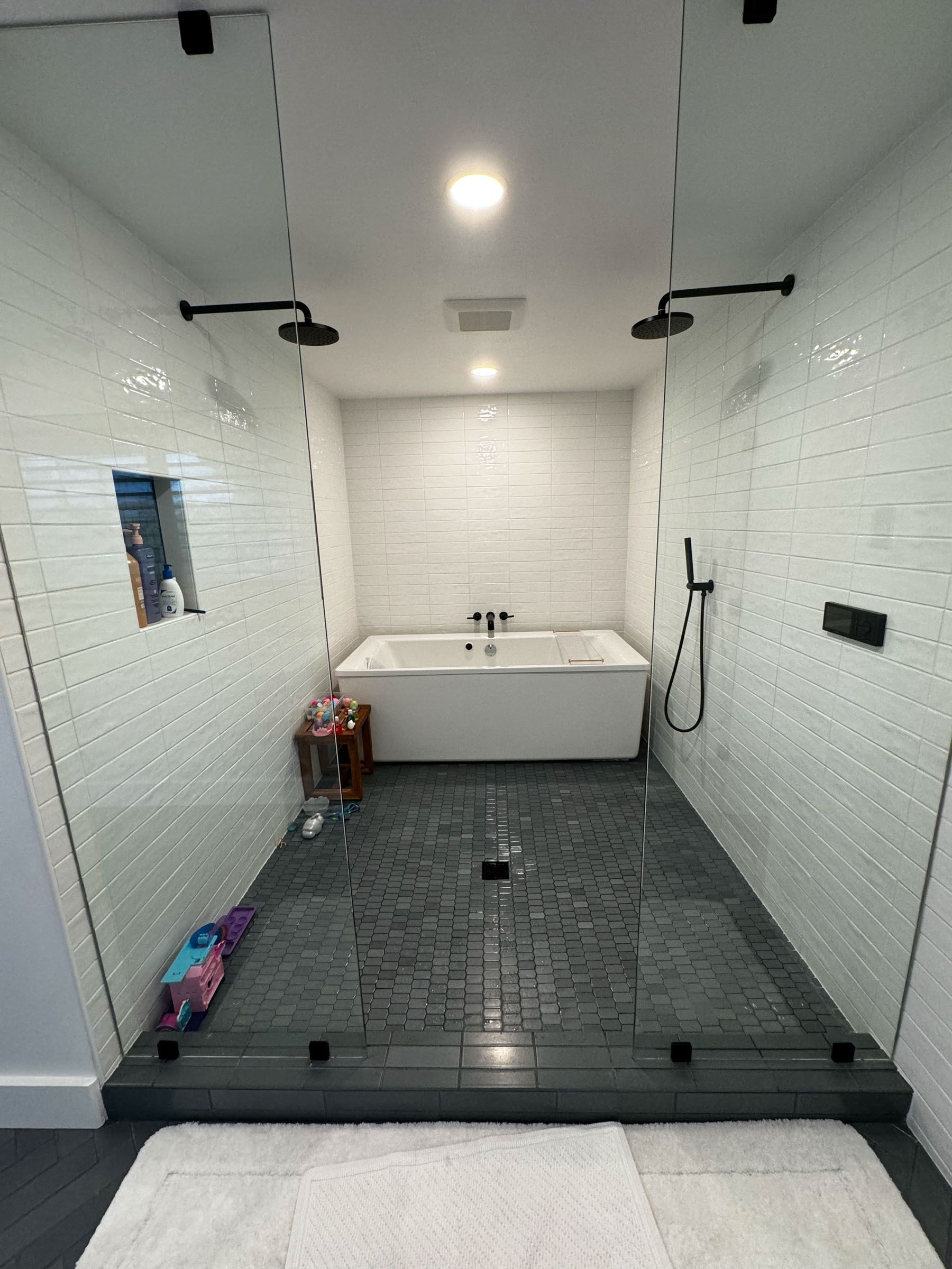 Modern walk-in shower with white subway tile, dark floor tile, and built-in bathtub at the back.
