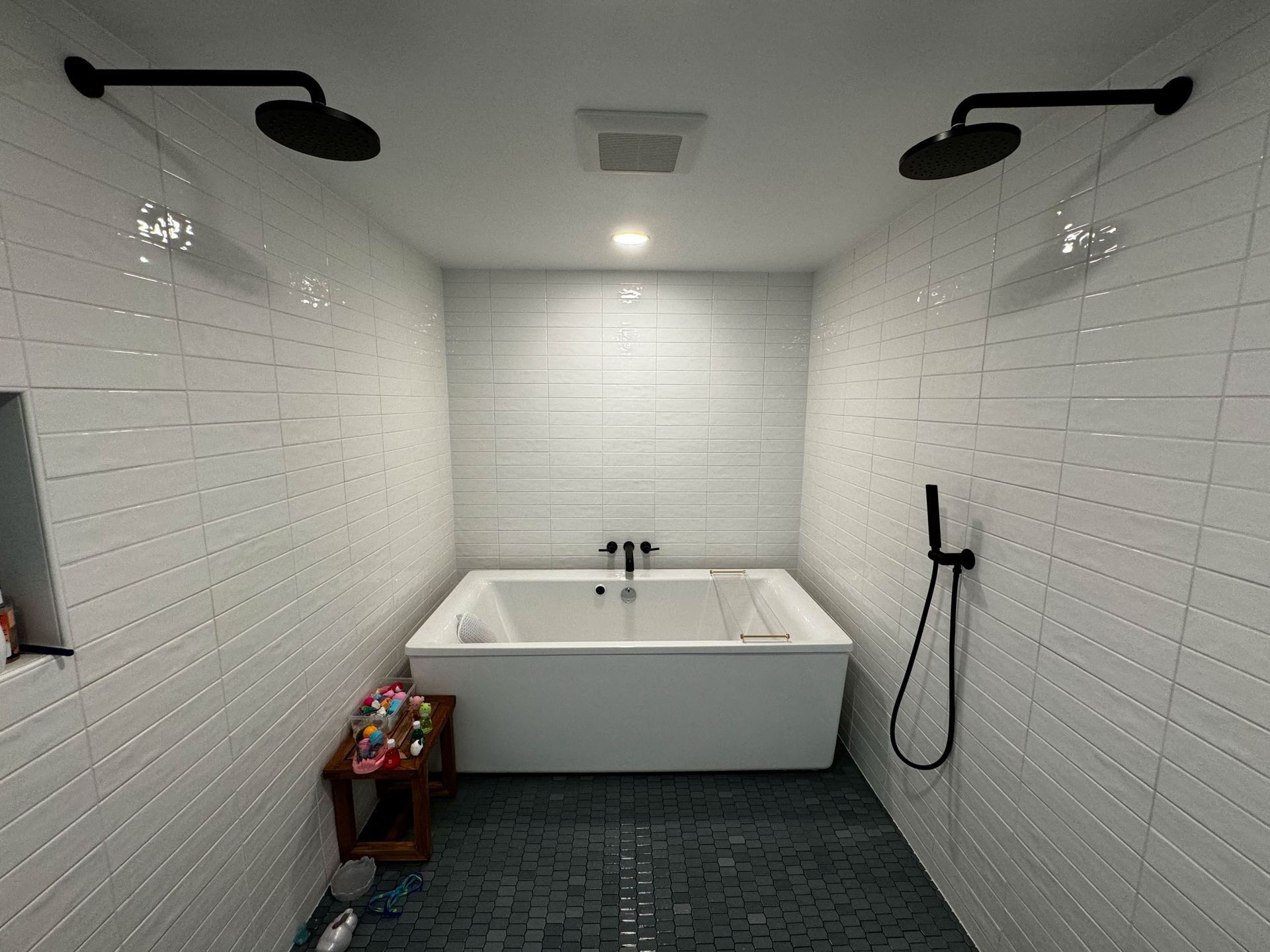 Bright white bathroom with a soaking tub, black wall showers, and dark tiled floor