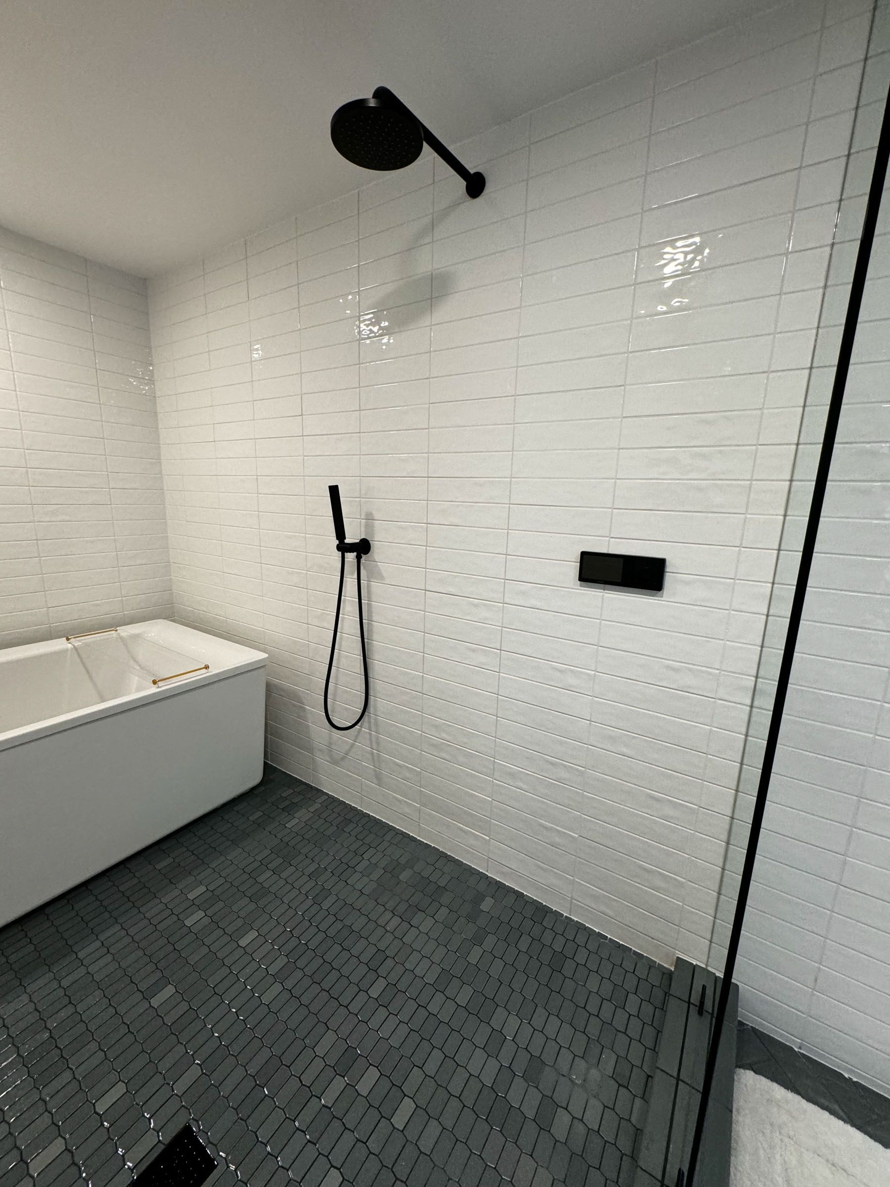 Modern bathroom shower with white tile walls, black fixtures, a freestanding tub, and dark mosaic floor.