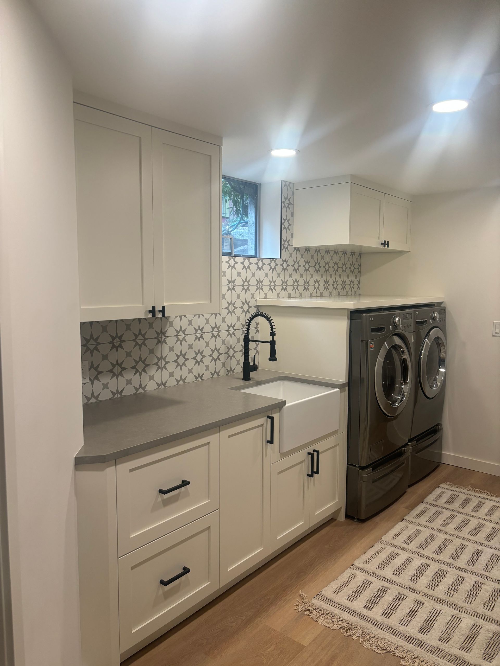 Compact laundry room with white cabinets, sink, patterned backsplash, and stacked washer-dryer.