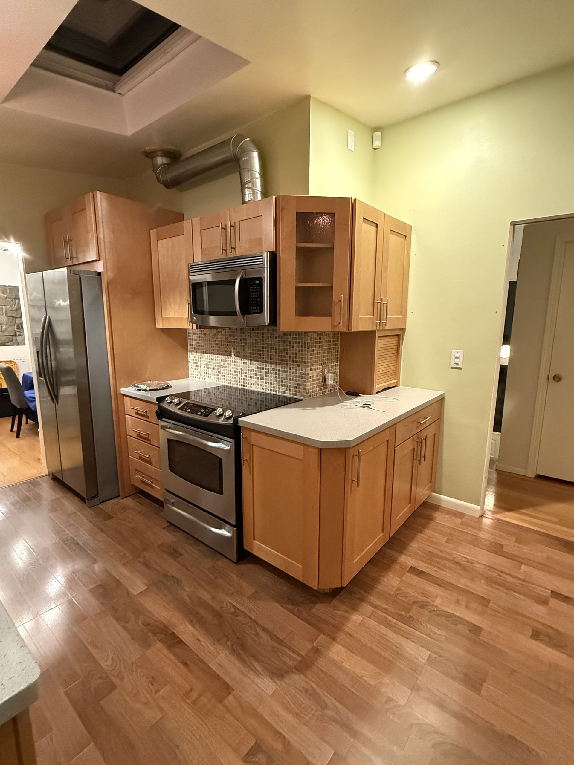 Kitchen with stainless steel appliances, wood cabinets, and hardwood floors in warm lighting.