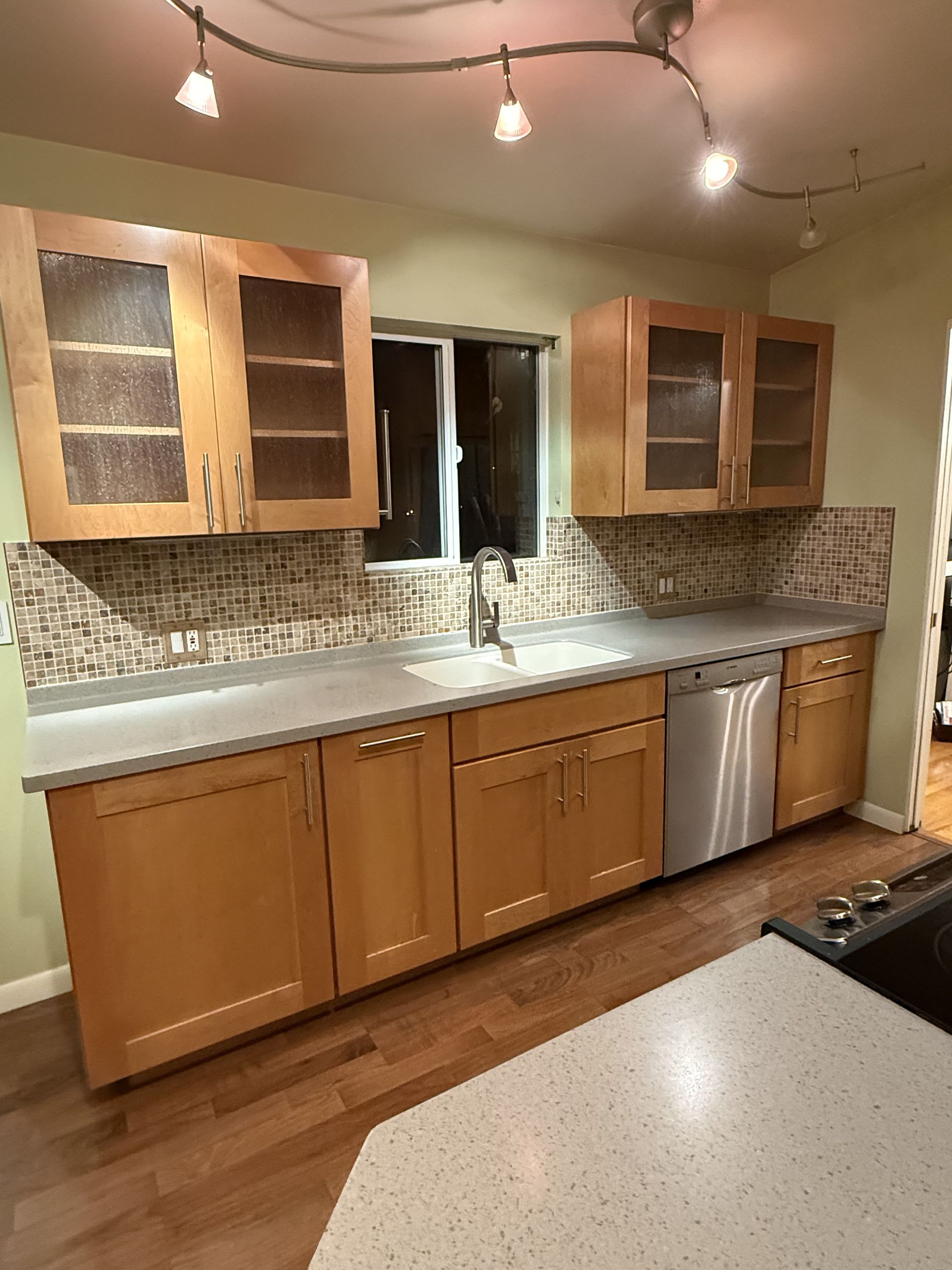 Modern kitchen with wood cabinets, granite counters, mosaic backsplash, stainless dishwasher, and track lighting.