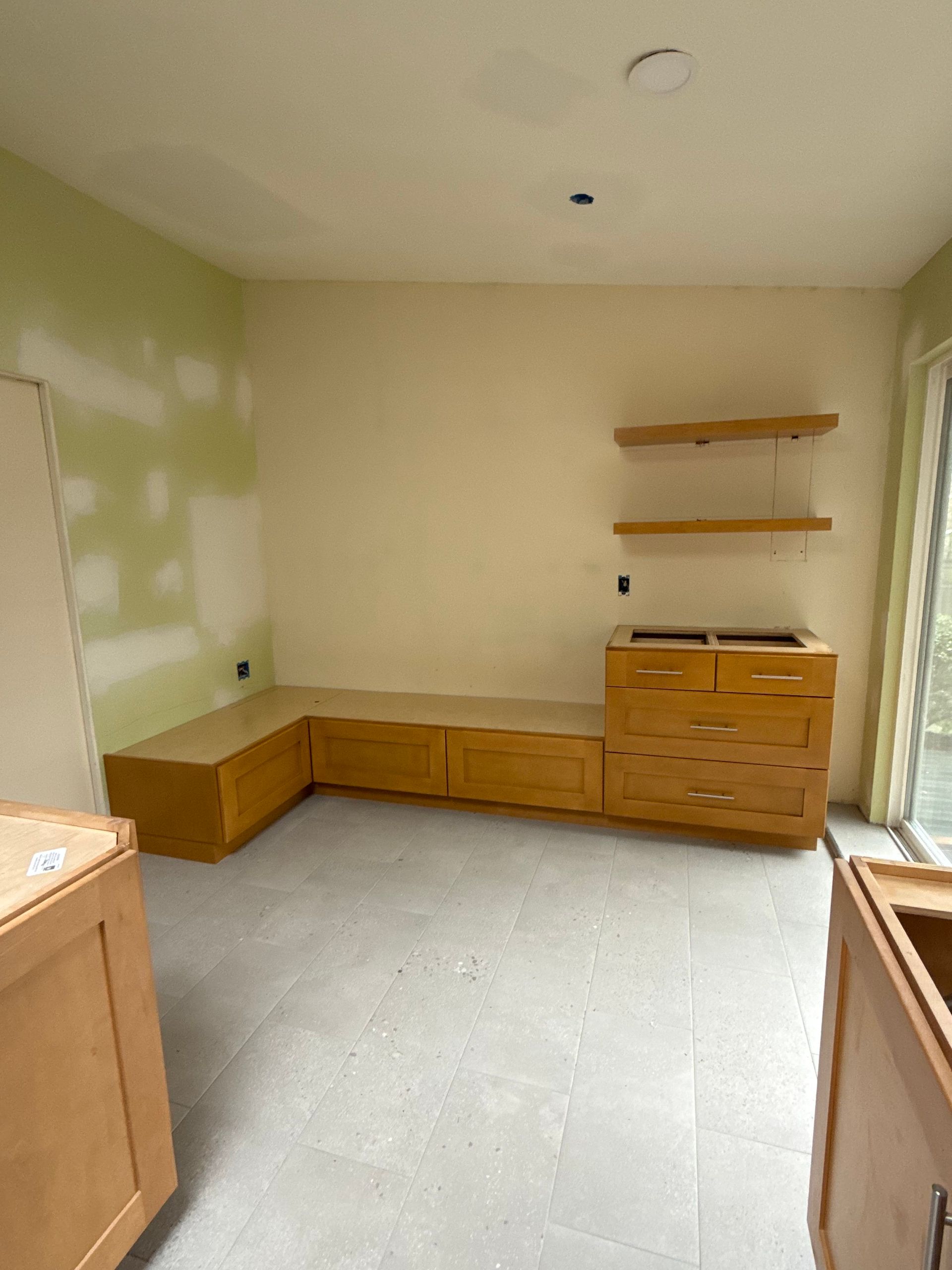 Empty room with built-in wood cabinets, two wall shelves, and unfinished green-and-beige walls.