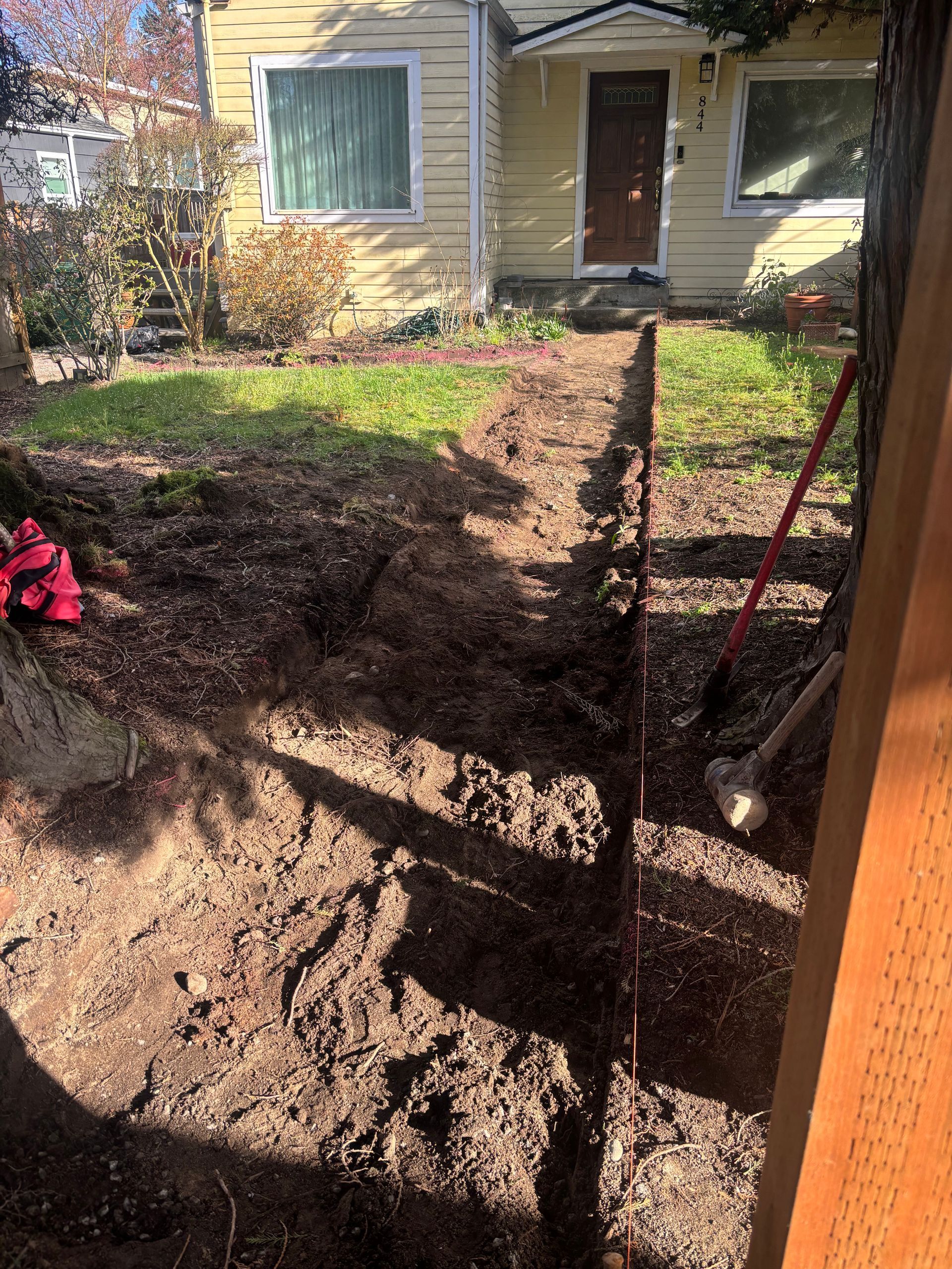 Backyard dirt path leading to a house doorway, with a fence and garden bed on the right.