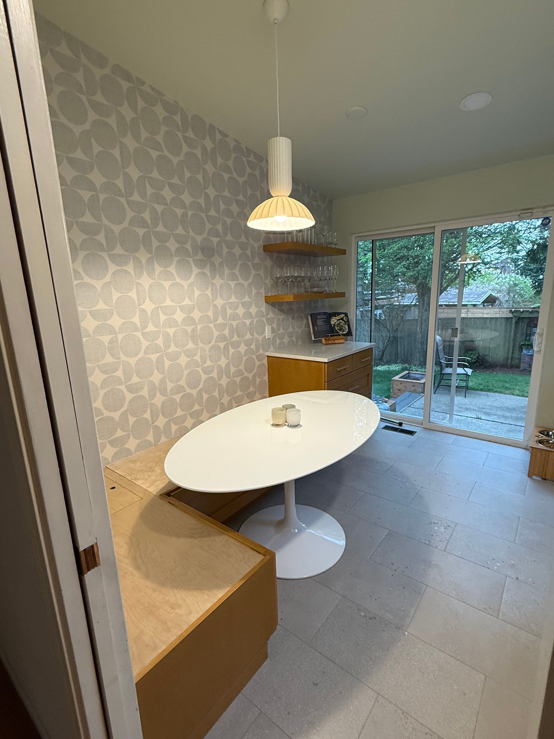 Modern dining nook with oval white table, pendant light, and sliding glass doors to a backyard.