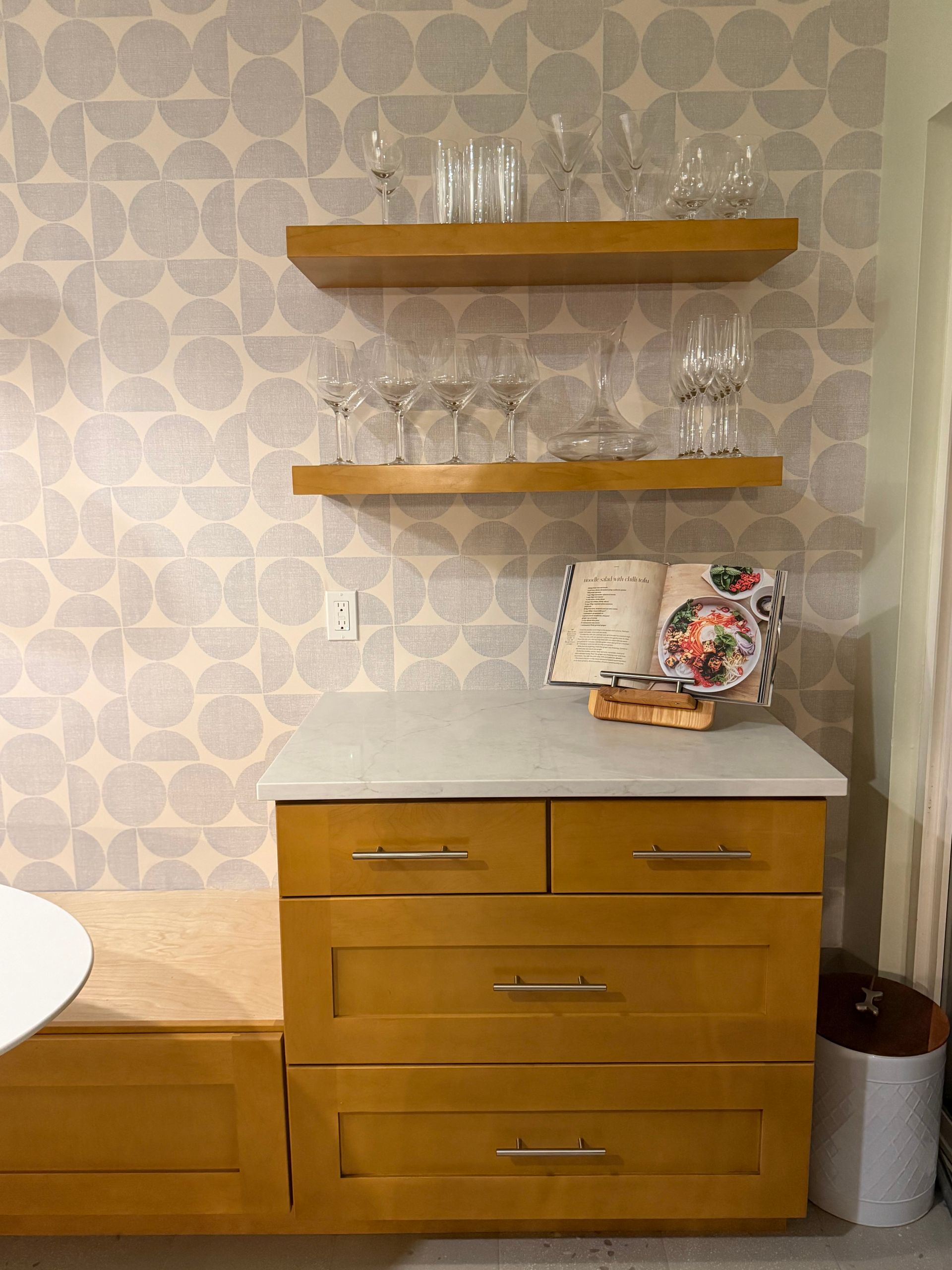 Wooden bathroom vanity with marble top, glass shelves, and a patterned wall