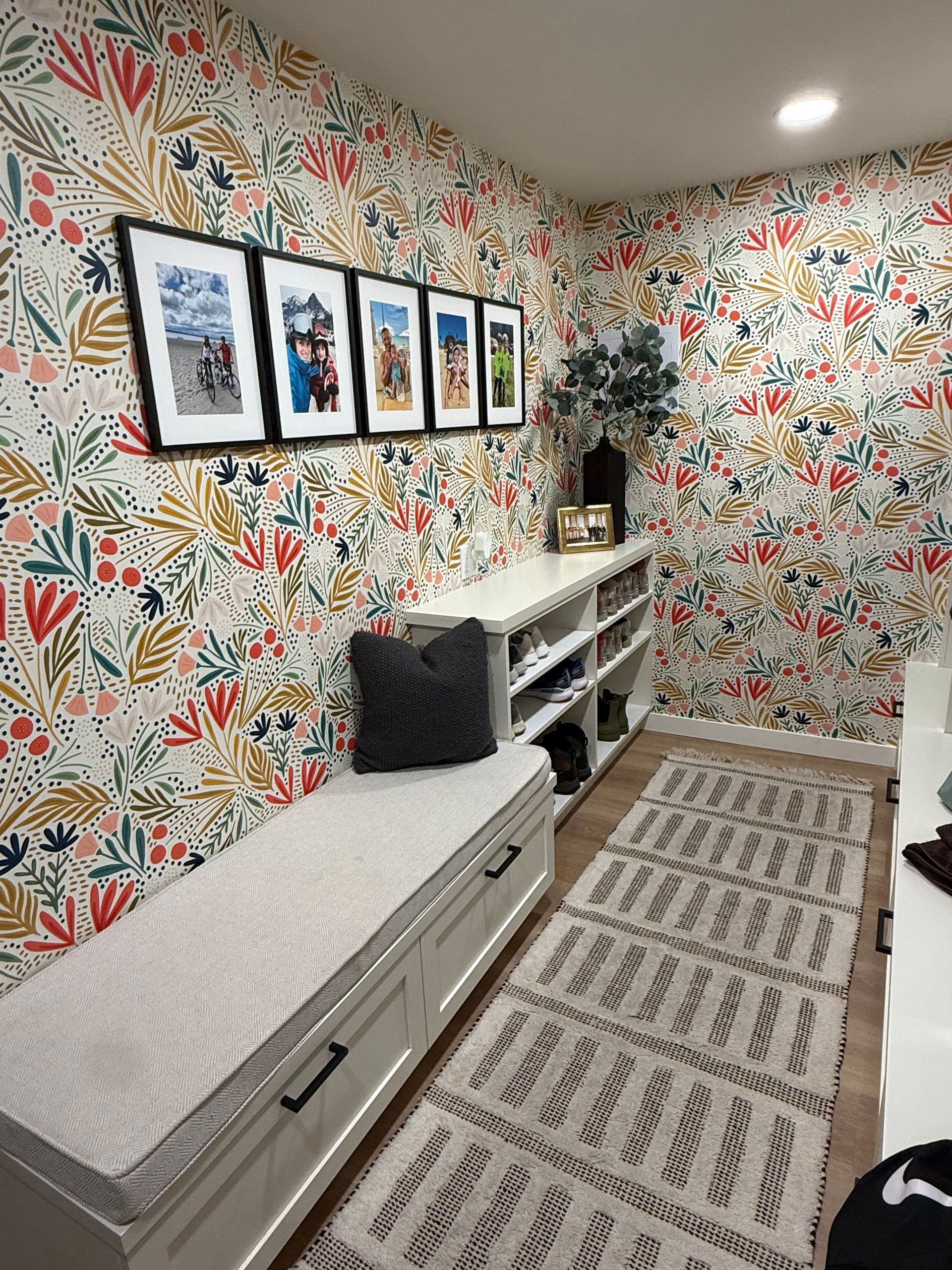 Bright home office with floral wallpaper, framed photos, a desk, storage cabinet, and patterned rug.
