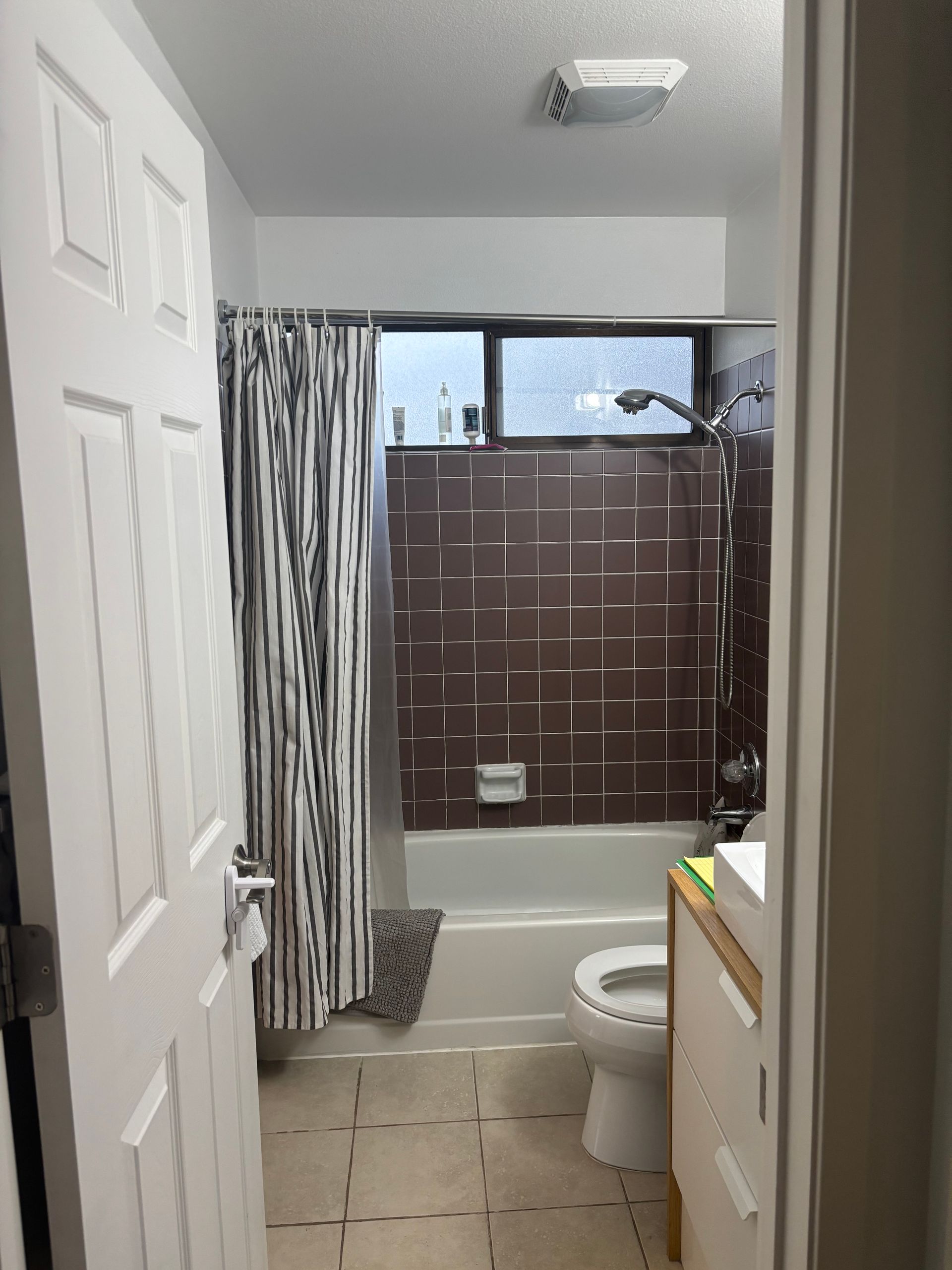 Small bathroom with shower curtain, toilet, vanity, and white door viewed from the hallway.
