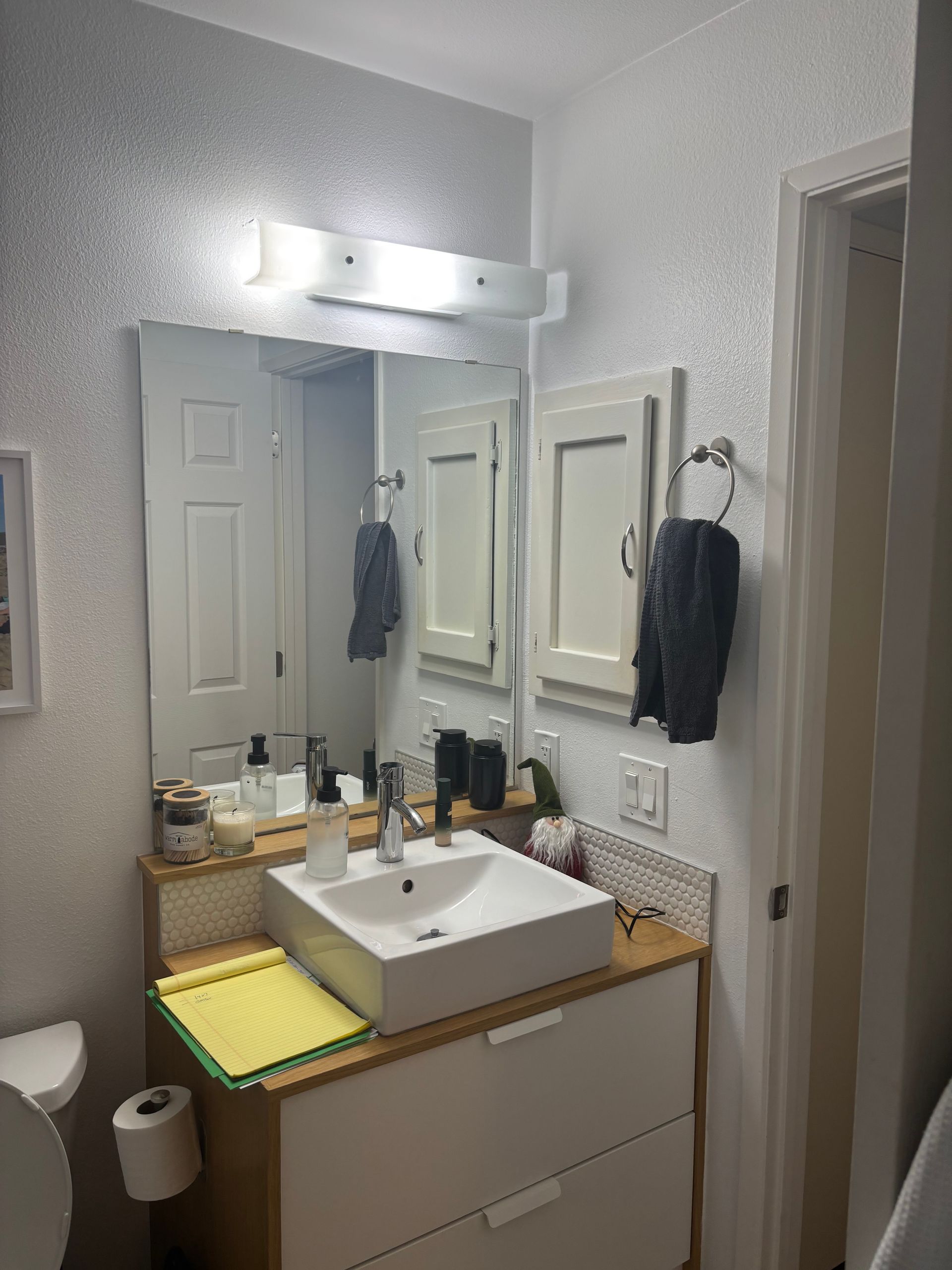 Bathroom vanity with mirror, white sink, and towels in a small tiled room