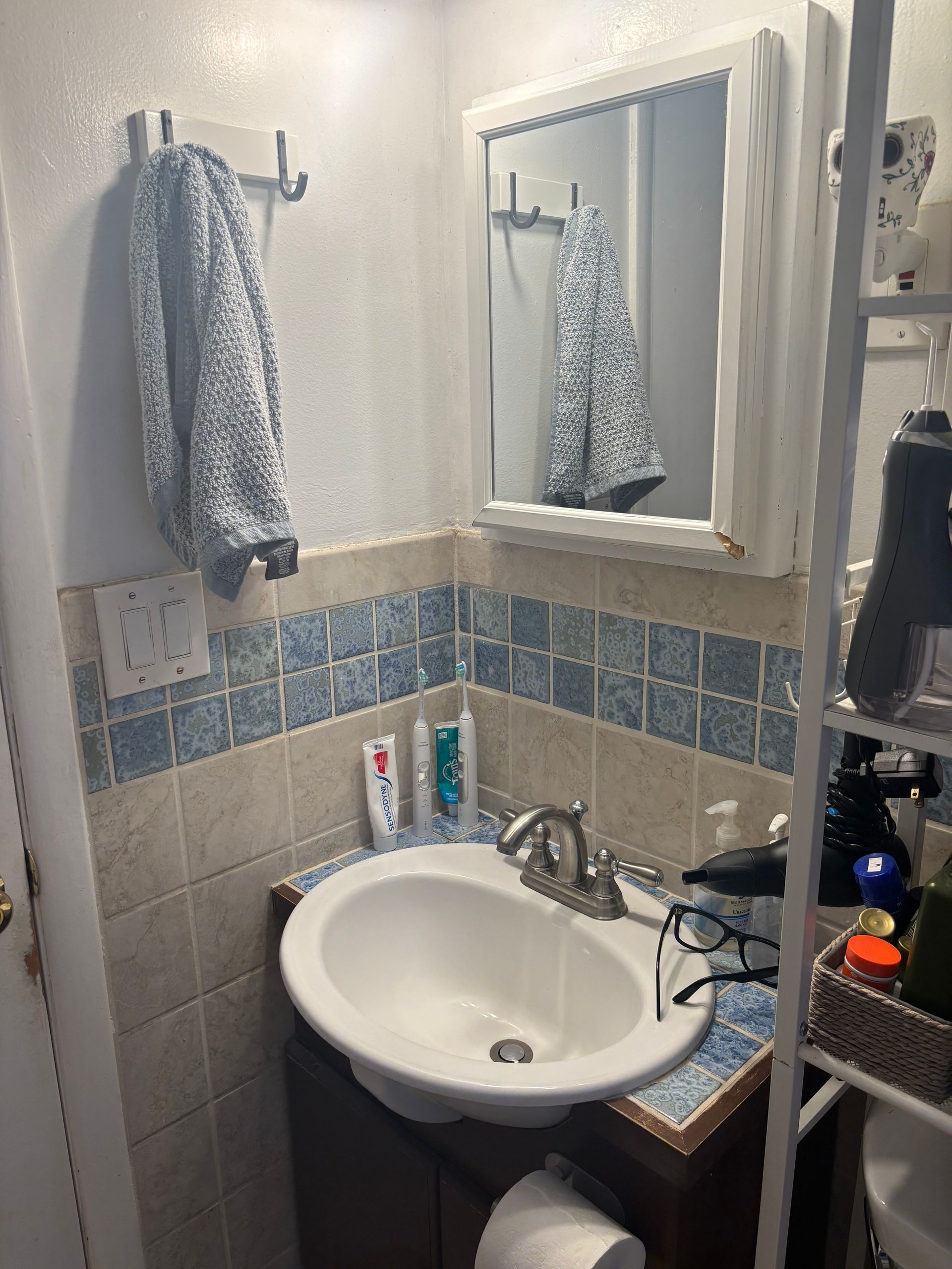 Small bathroom with white sink, mirror cabinet, blue tile trim, and a towel hanging on the wall.