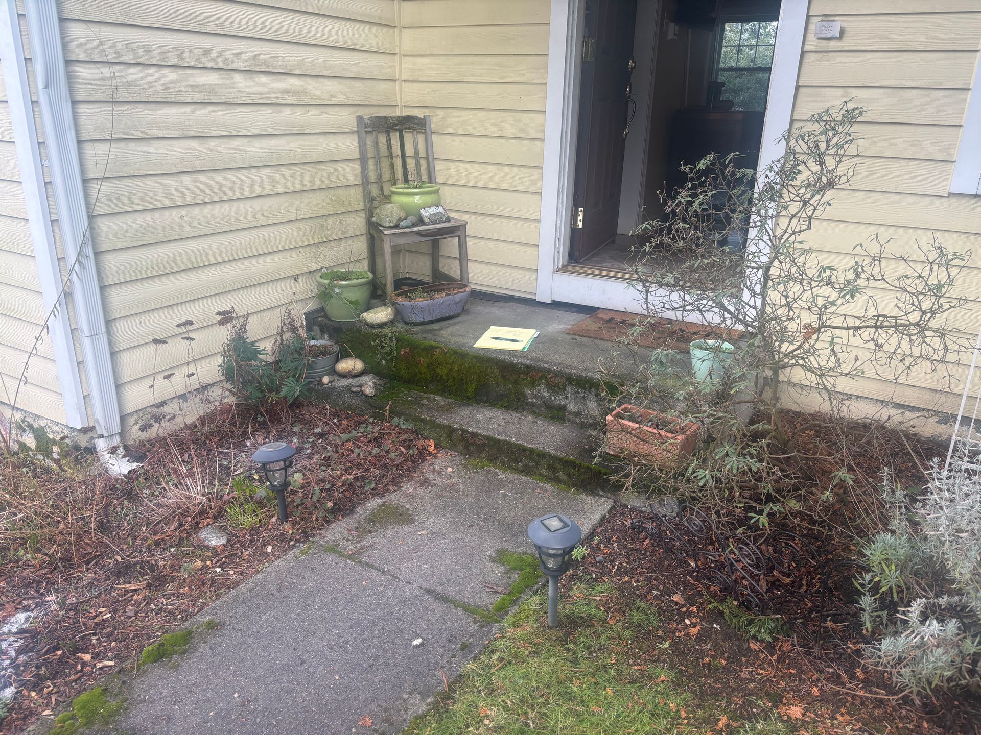 Front porch with weathered steps, potted plants, and a glass storm door at a beige house