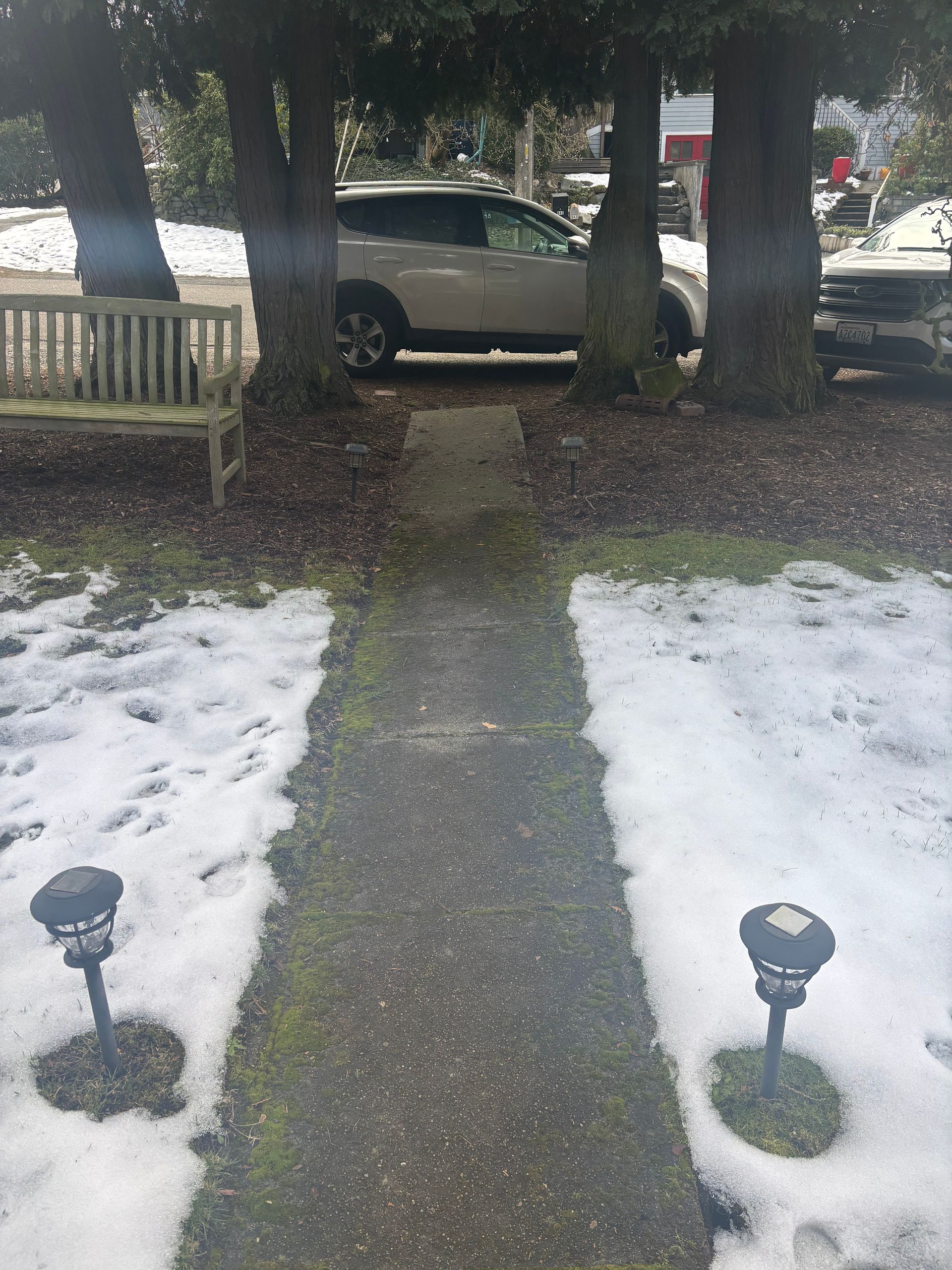 Snow-dusted front yard path leading to a parked silver car under trees