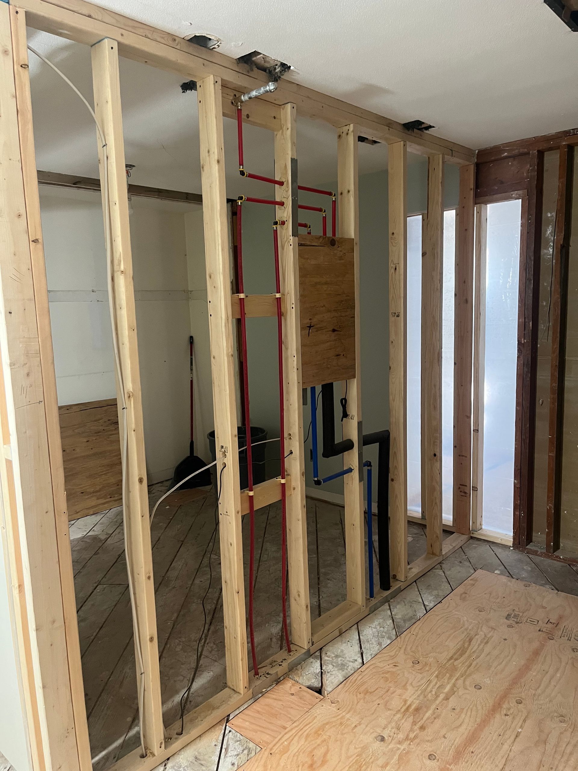 Framed interior wall under construction with exposed studs, plumbing, and subflooring in a room