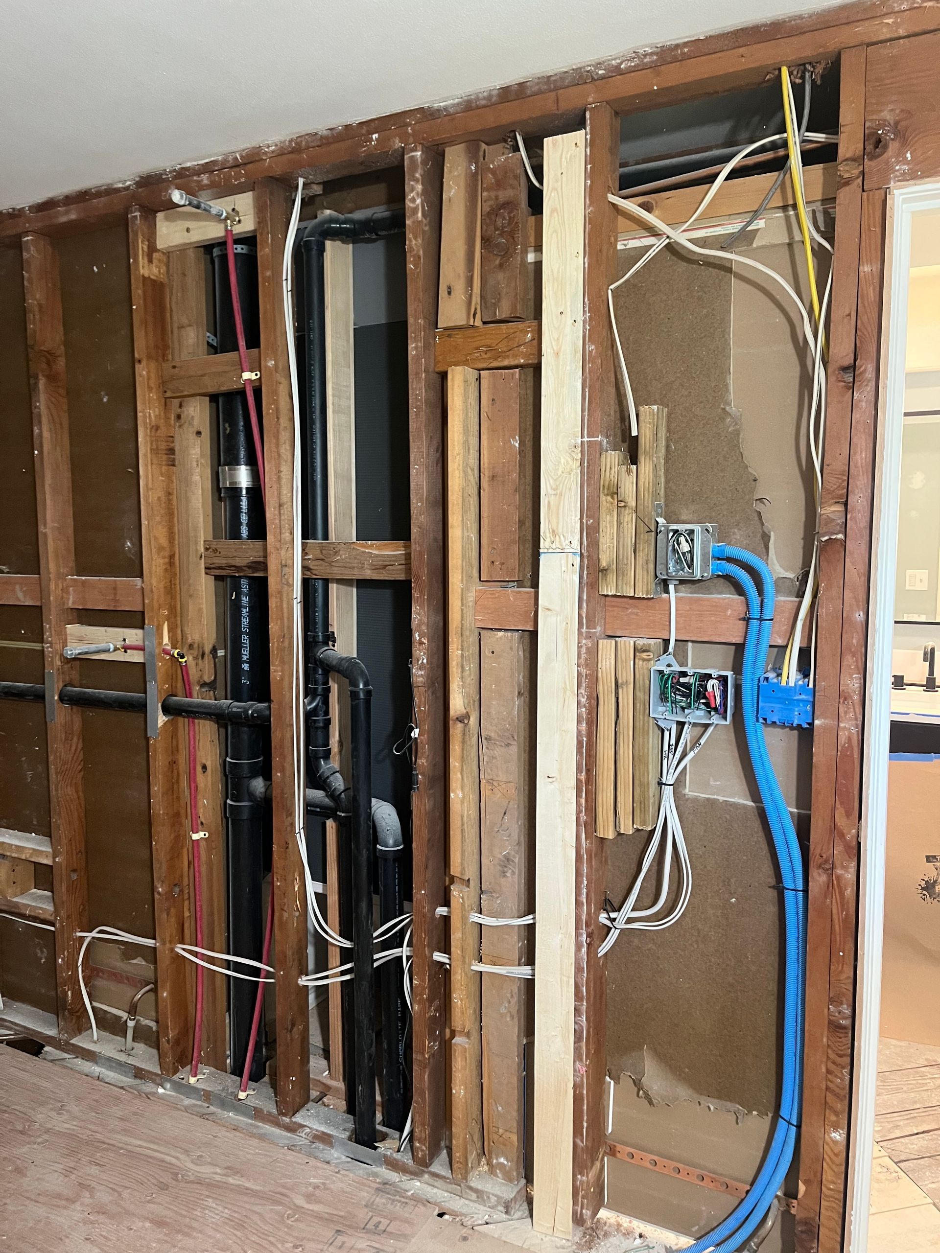 Exposed wall studs with visible electrical wiring, blue cables, and open junction boxes during renovation
