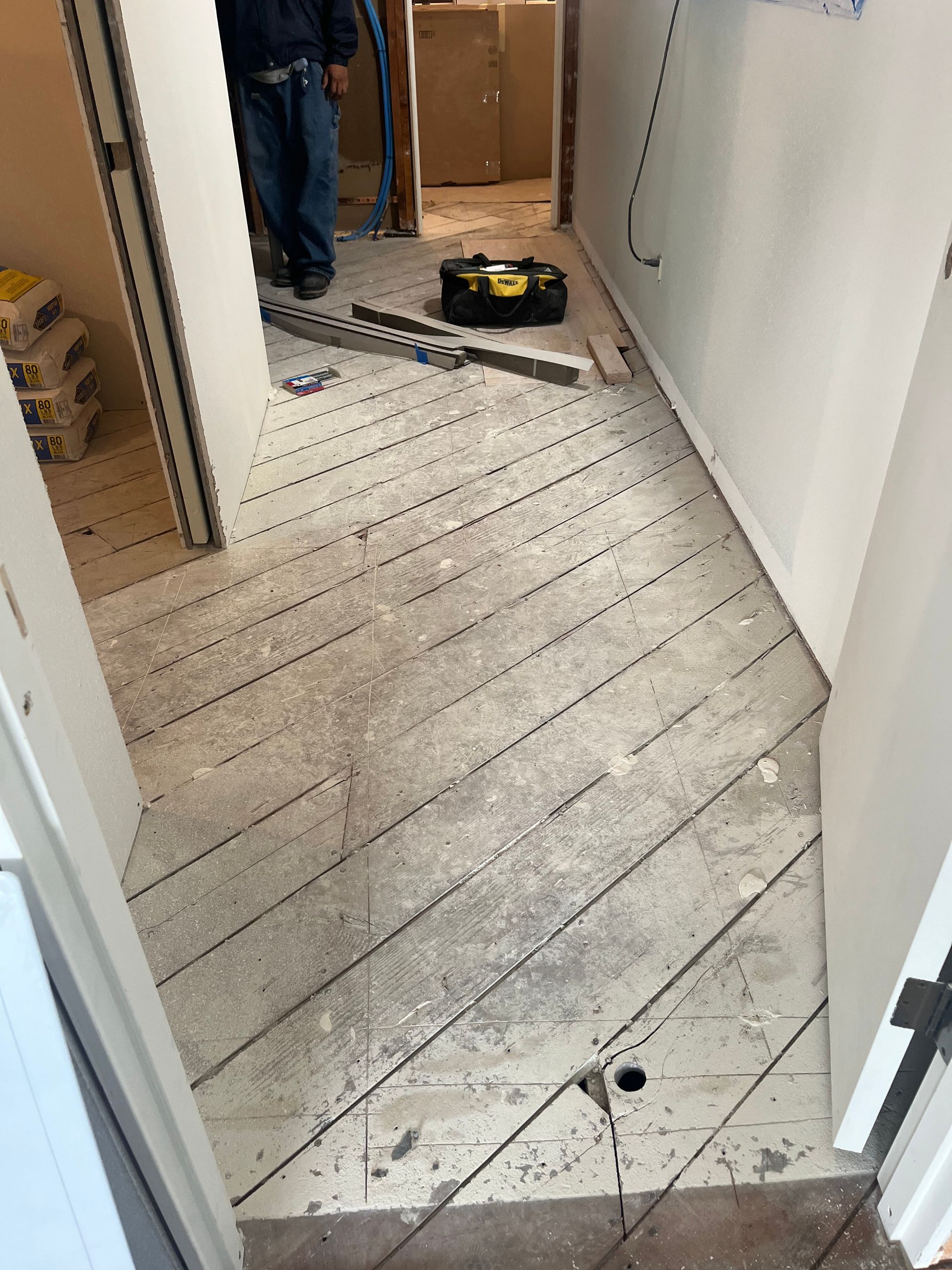 Hallway with stripped floorboards, doorway, and a yellow tool on the floor during renovation