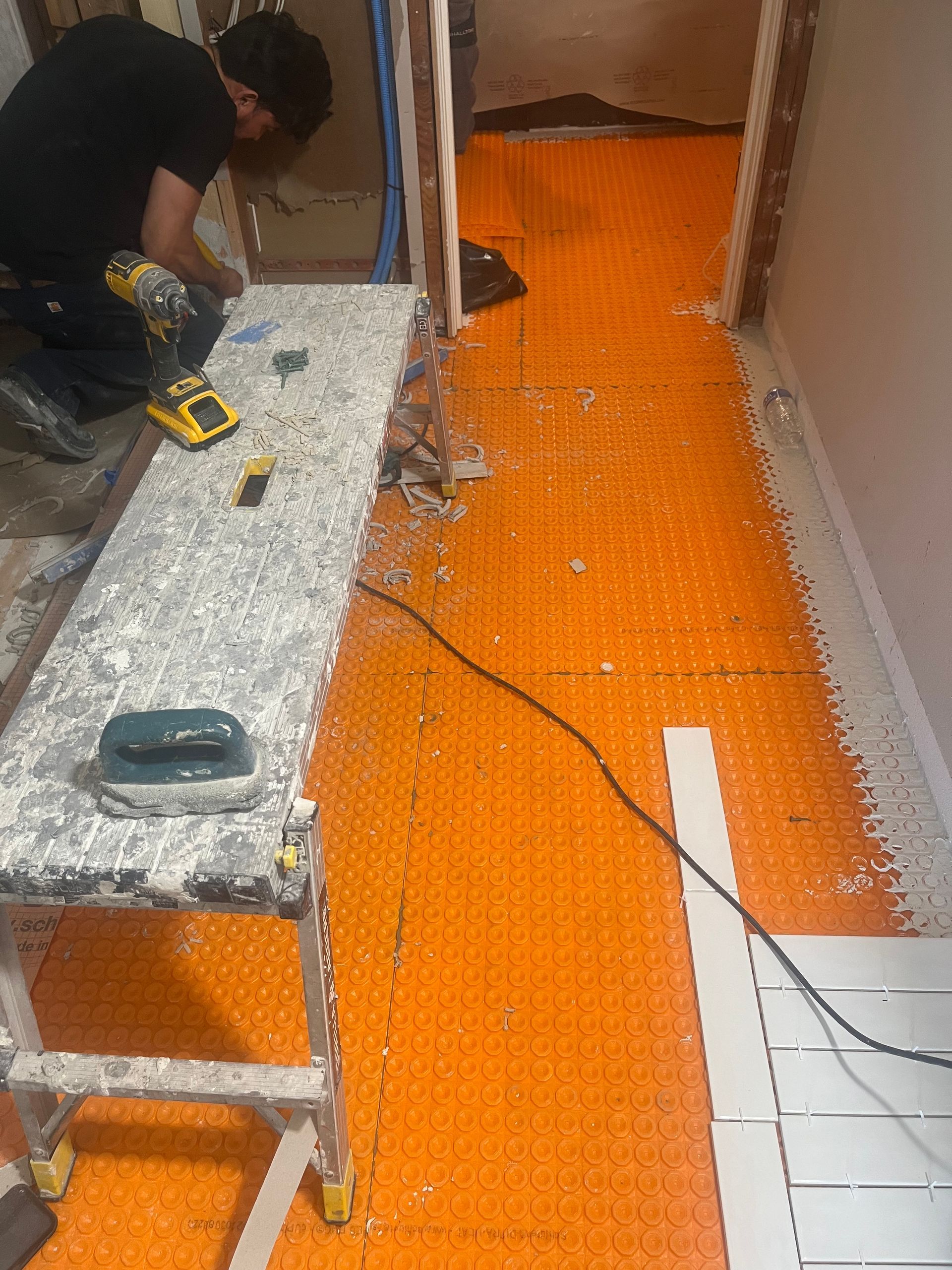 Worker installing orange underlayment in a hallway during floor renovation