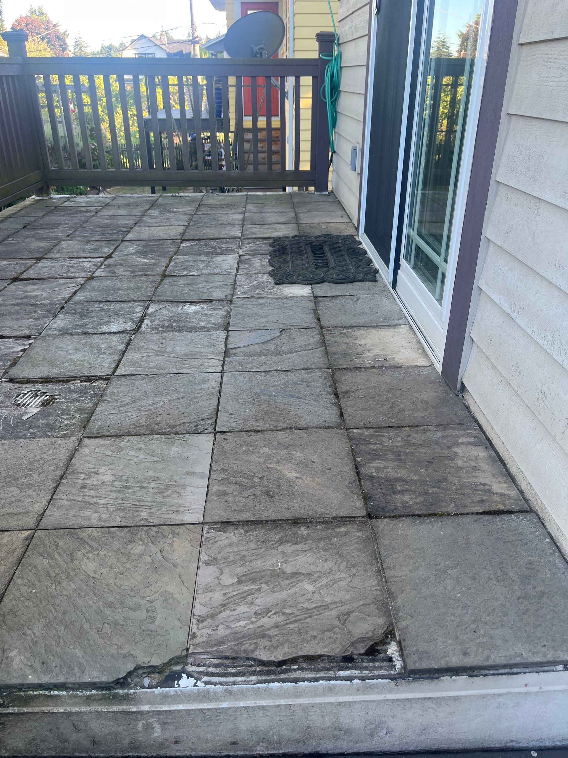 Cracked patio pavers beside a house, leading to a wooden gate and fence.