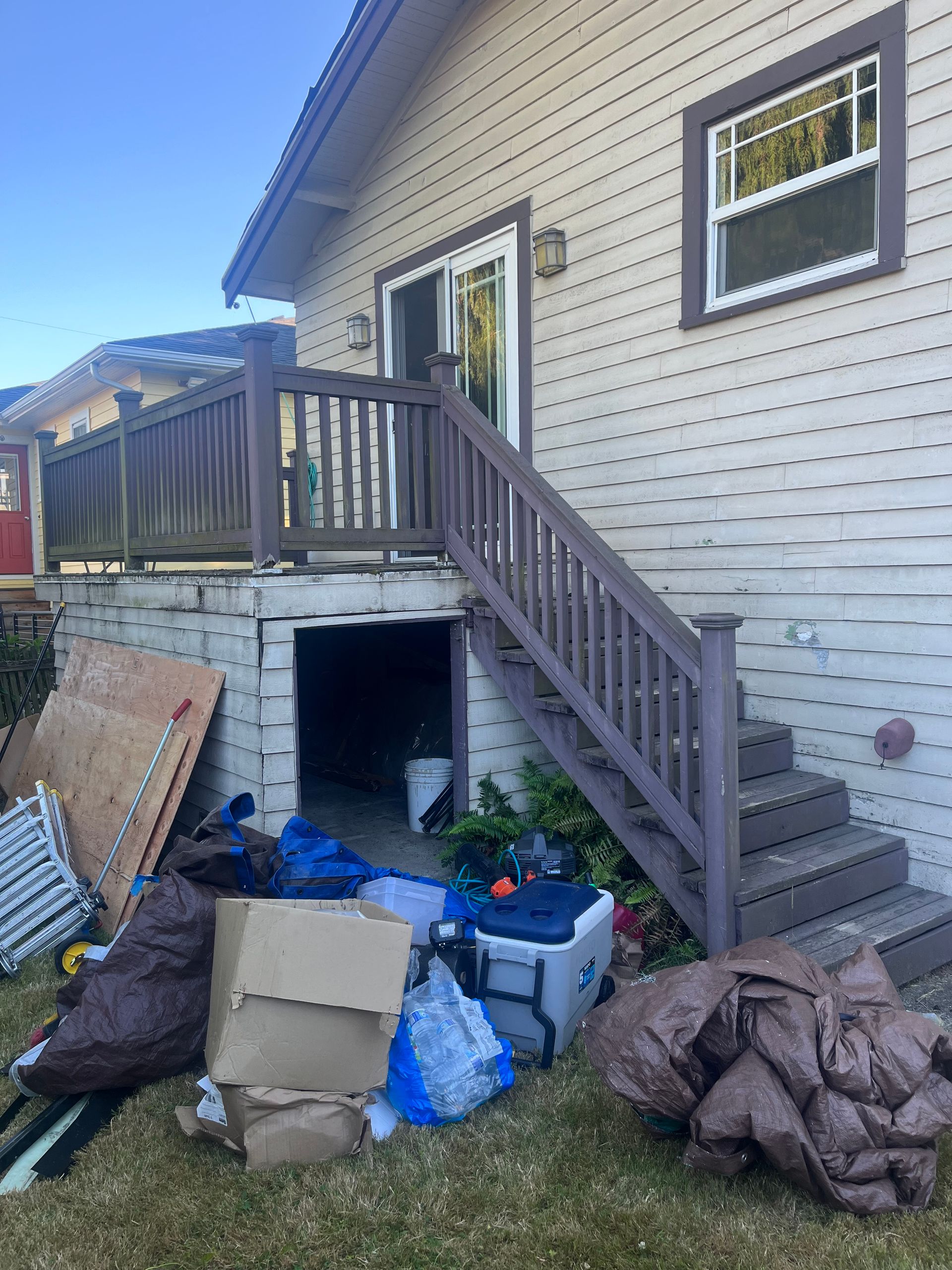 Side view of a house with exterior stairs, deck, and debris piled below the deck.