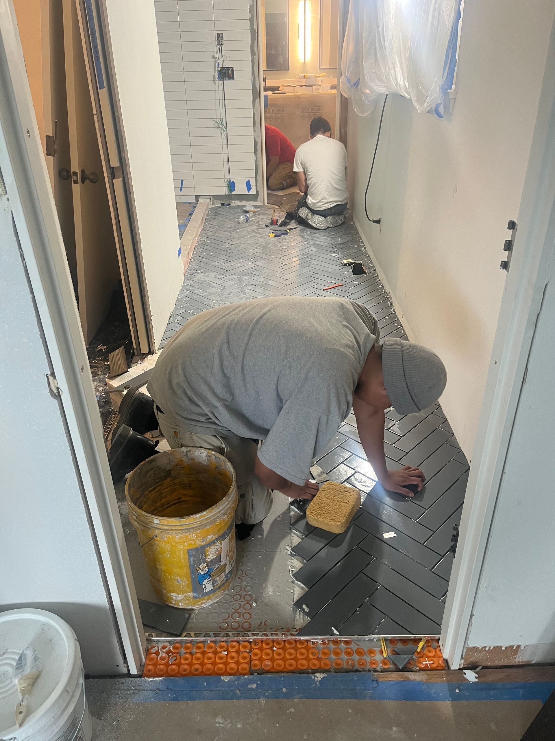 Workers installing flooring in a narrow hallway, with tools and materials scattered on the floor.