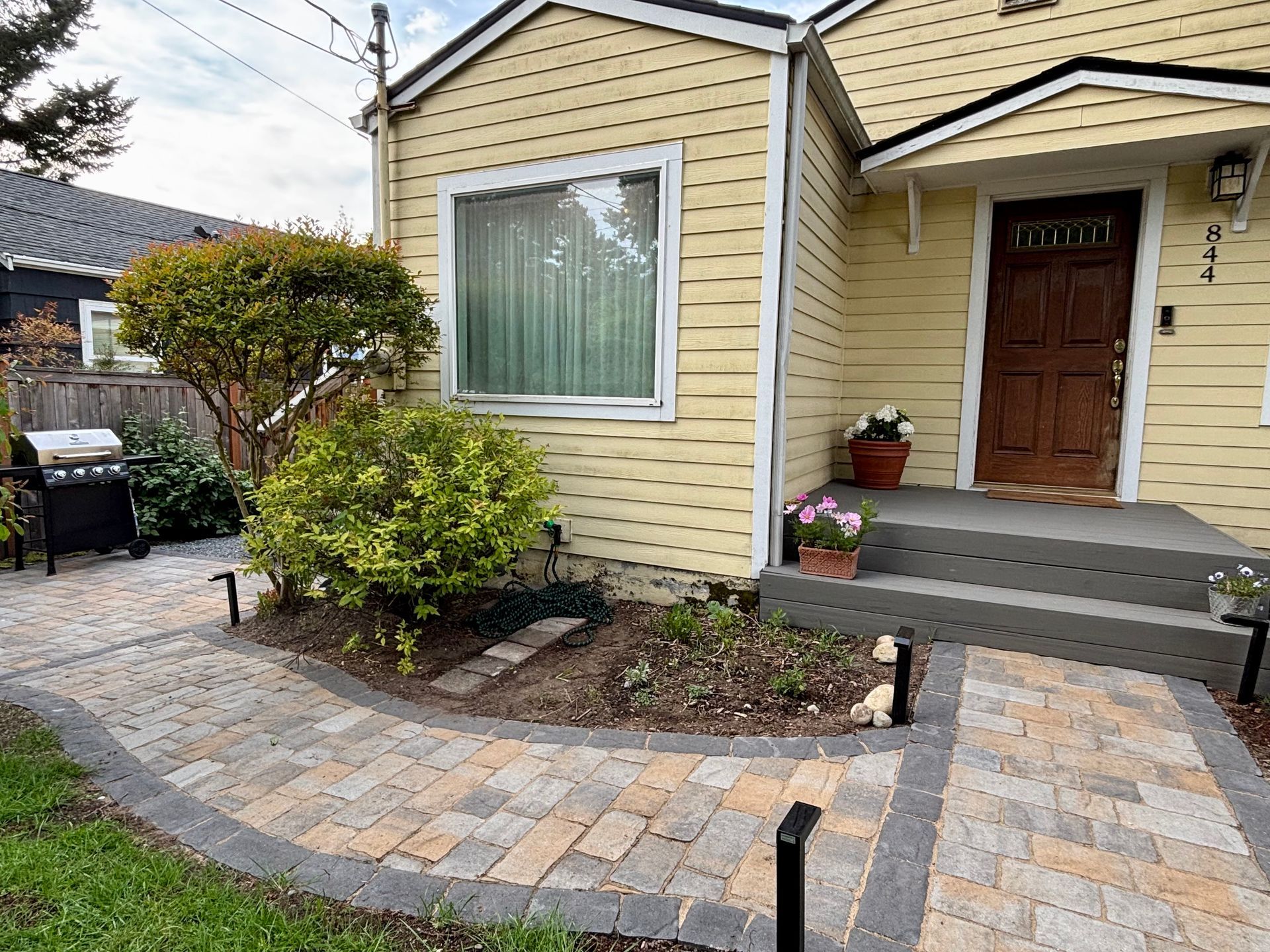 Front of a yellow house with a wooden door, front porch, and landscaped stone walkway and garden