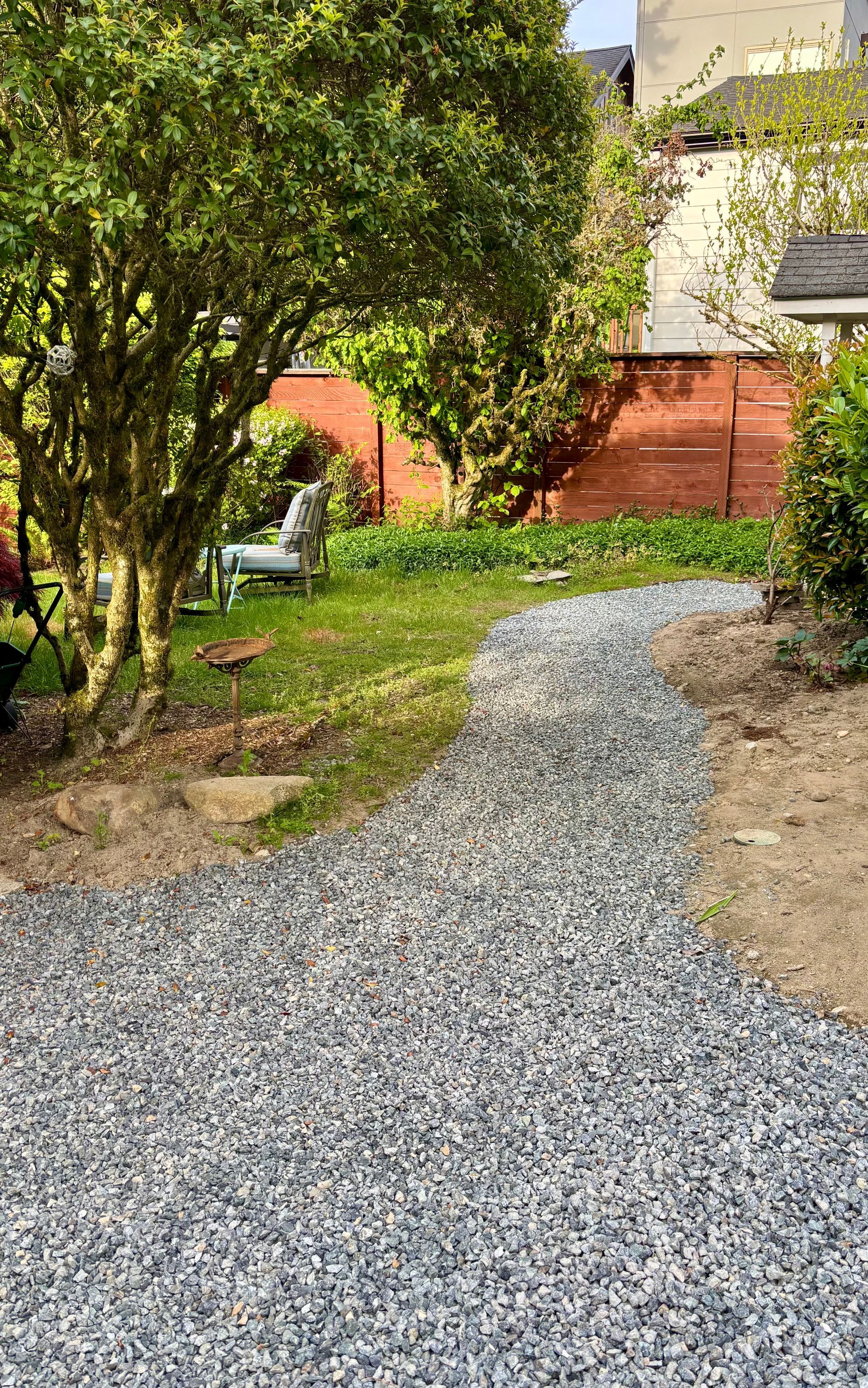 Gravel garden path leading through trees and shrubs to a red fence and house