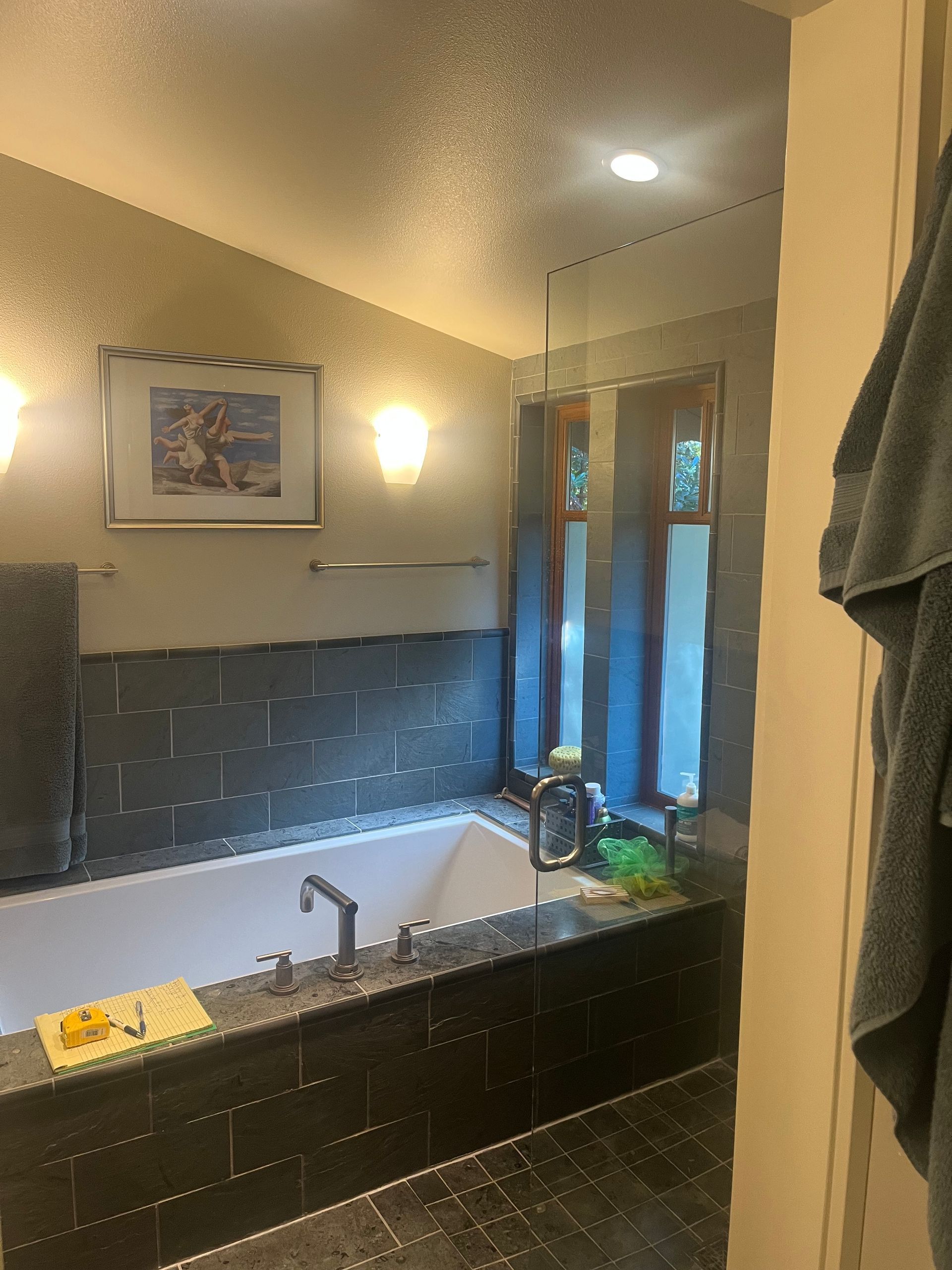 Bathroom with black tile vanity, sink, mirror, framed art, and towel hanging by the shower door