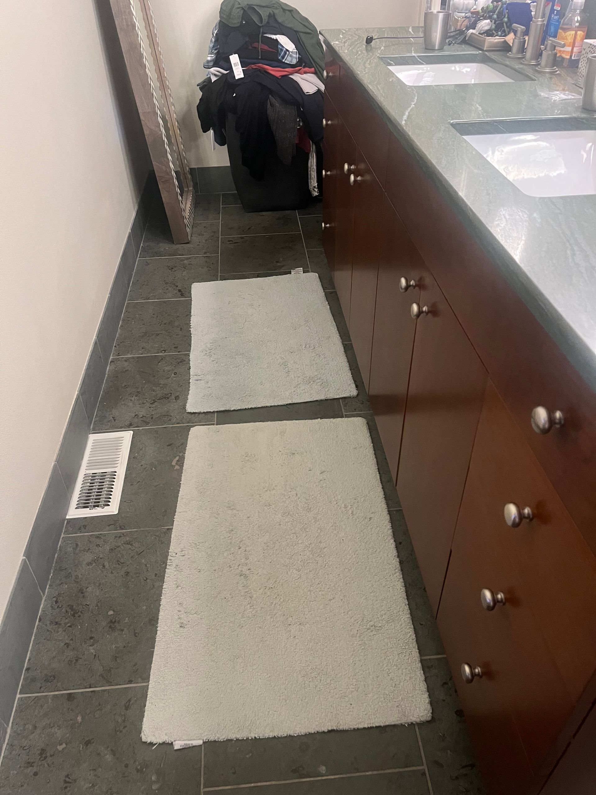 Bathroom floor with two white rugs, a wooden vanity, and a black bag near the end of the counter.