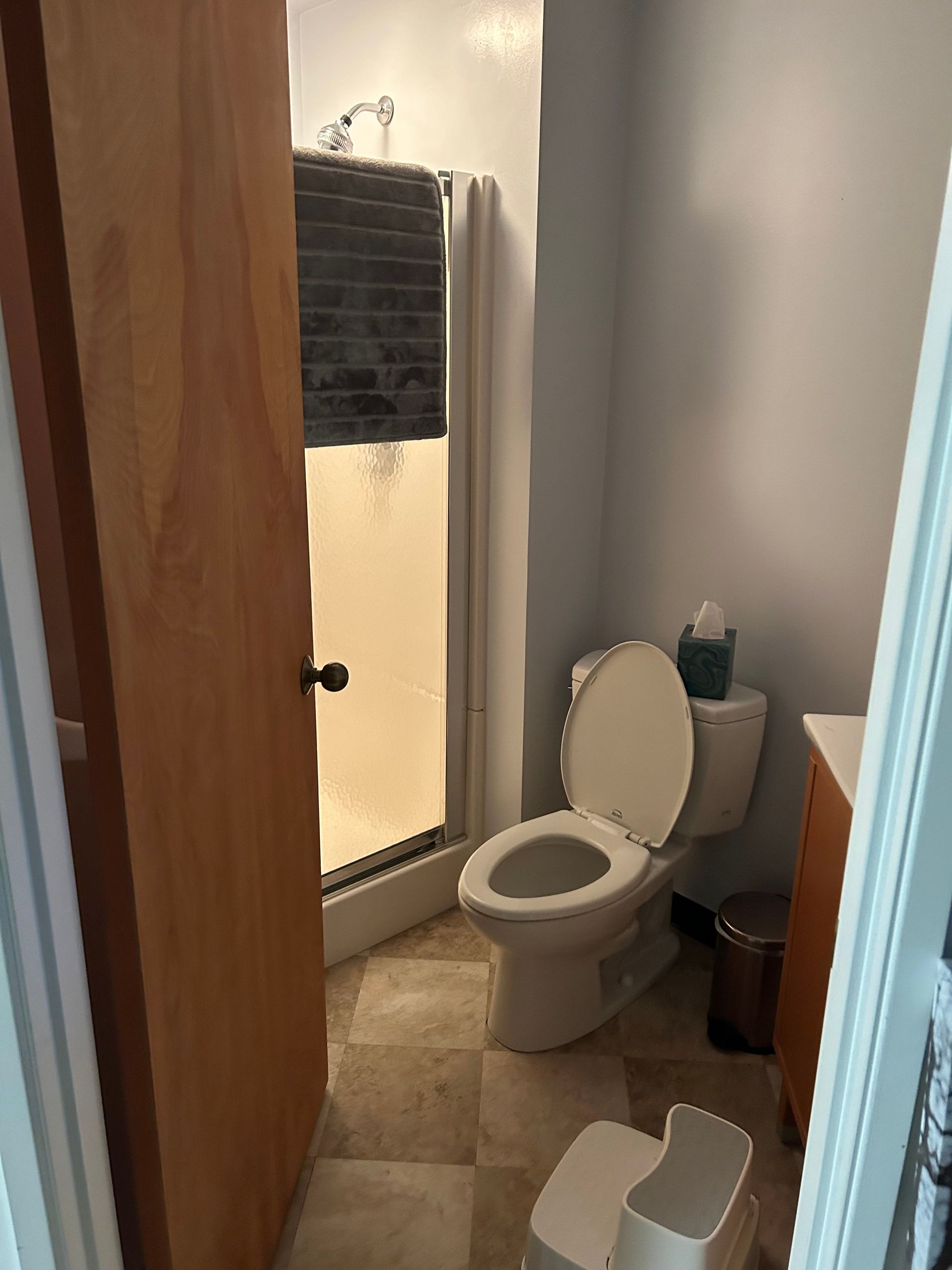 Small bathroom with an open toilet, shower, sink cabinet, and tiled floor.