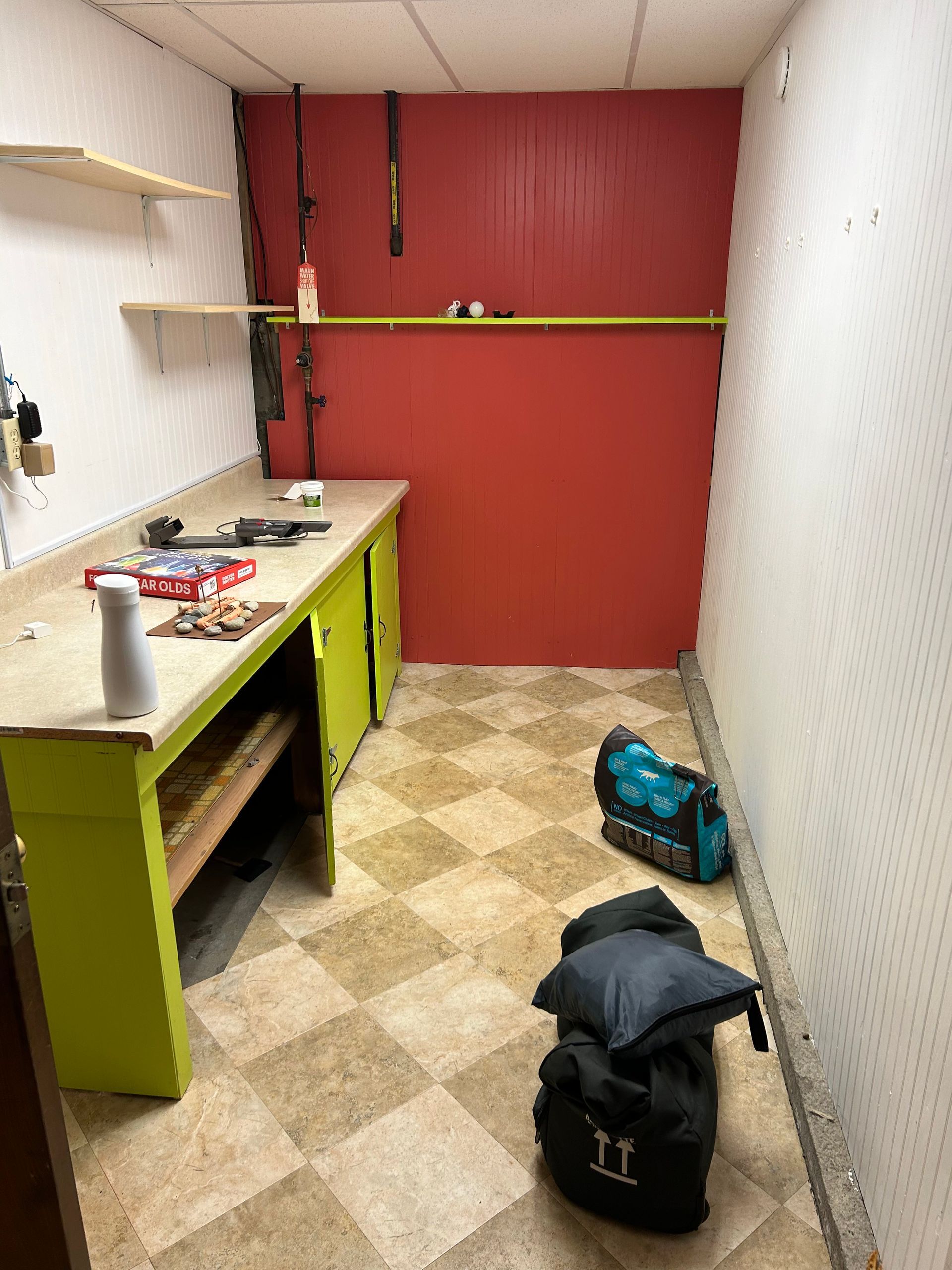 Small workshop with workbench, shelves, red back wall, and a backpack on the floor.