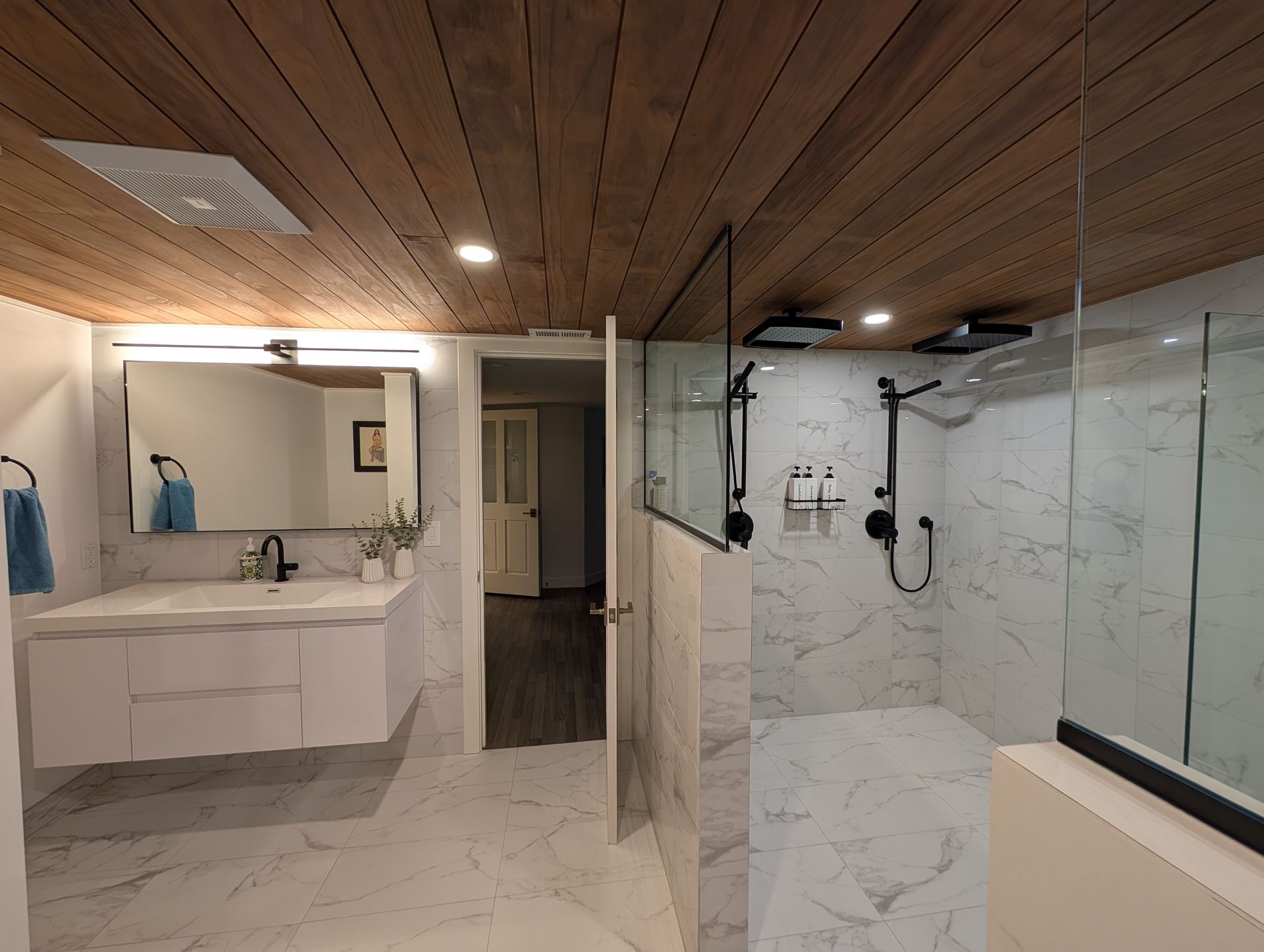 Modern bathroom with marble tile, wood ceiling, double vanity, mirror, and glass shower.