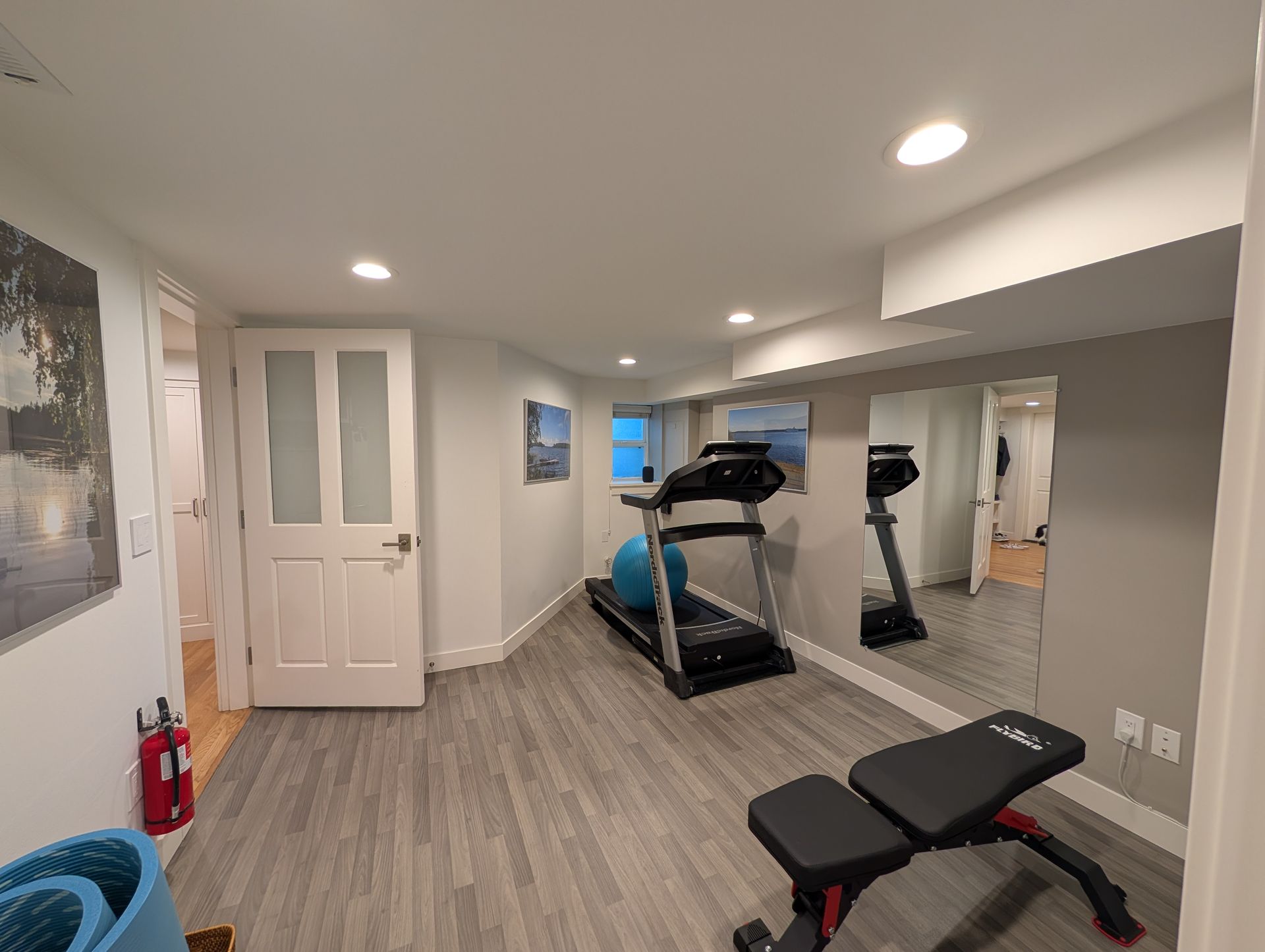 Home gym room with treadmill, wall mirror, exercise bench, and white door on wood floor