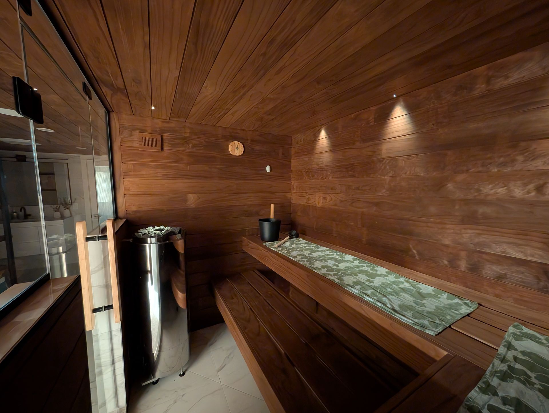 Wood-paneled sauna with wooden benches, green towels, and a stainless steel heater
