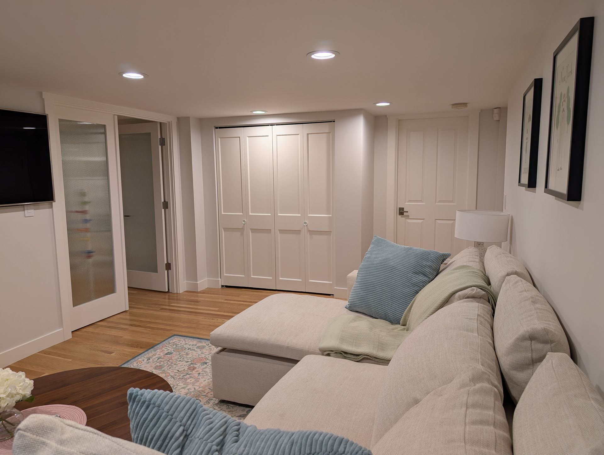 Cozy basement living room with beige sectional, blue pillows, recessed lights, and white closet doors