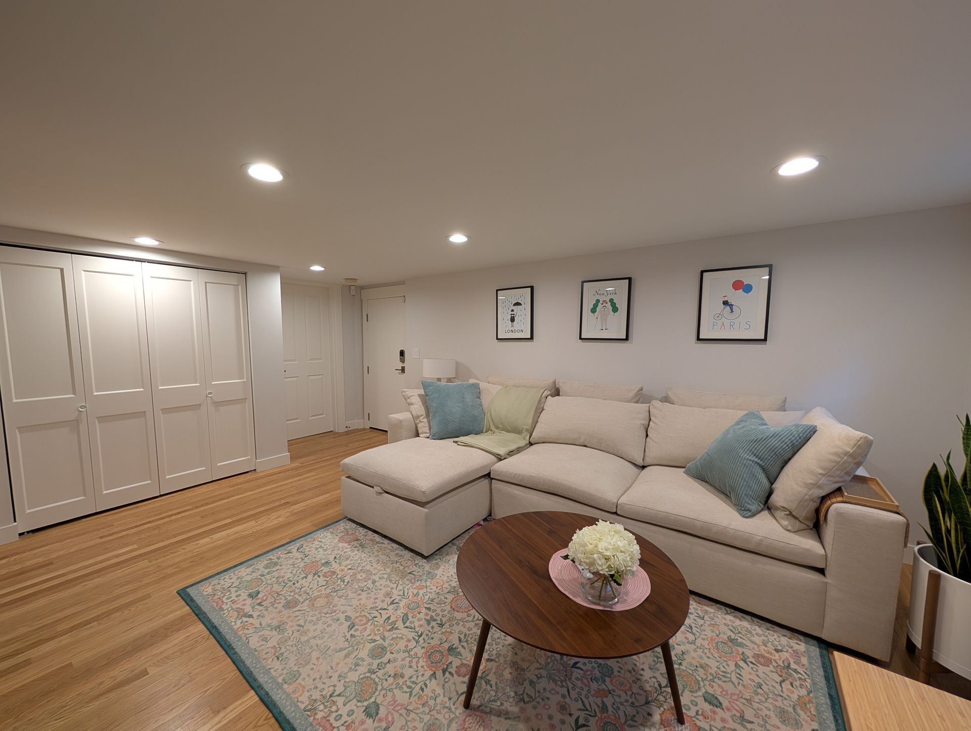 Bright living room with beige sectional, patterned rug, round coffee table, and recessed ceiling lights.