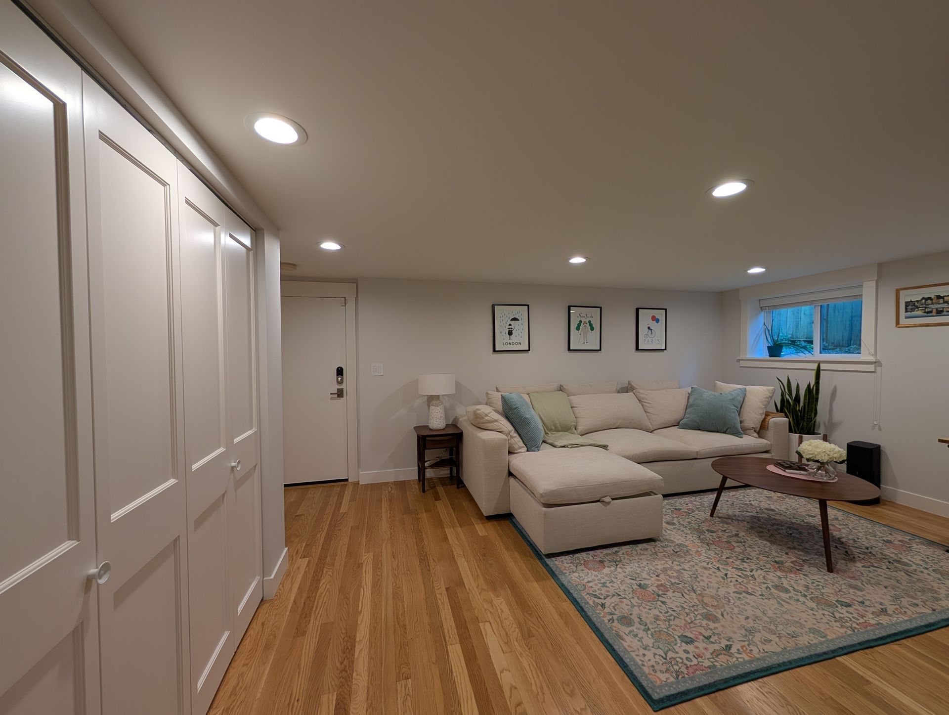 Bright living room with beige sectional sofa, patterned rug, wood floors, and wall art.