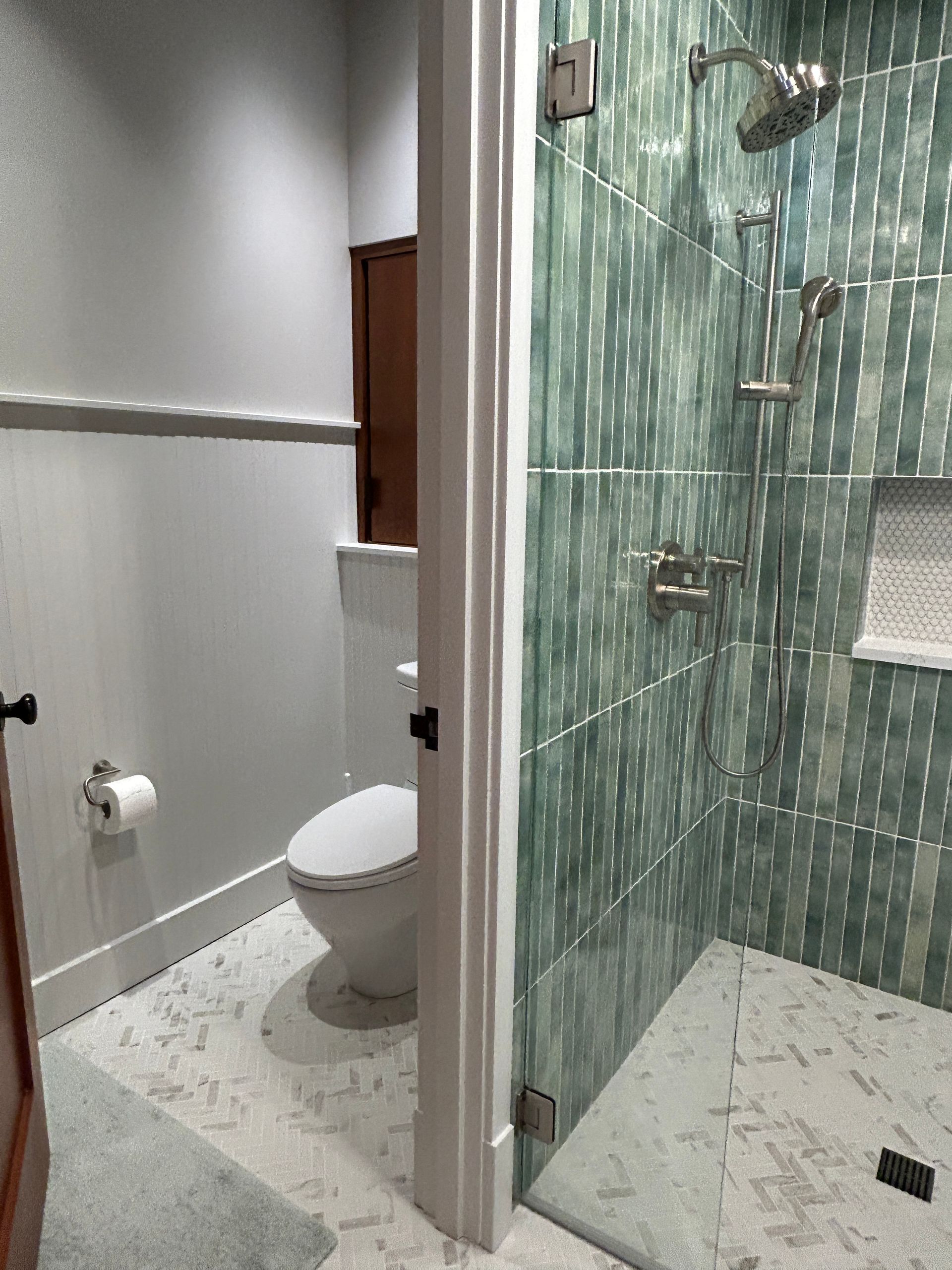Small bathroom with a toilet, sink, and walk-in glass shower with green tile.