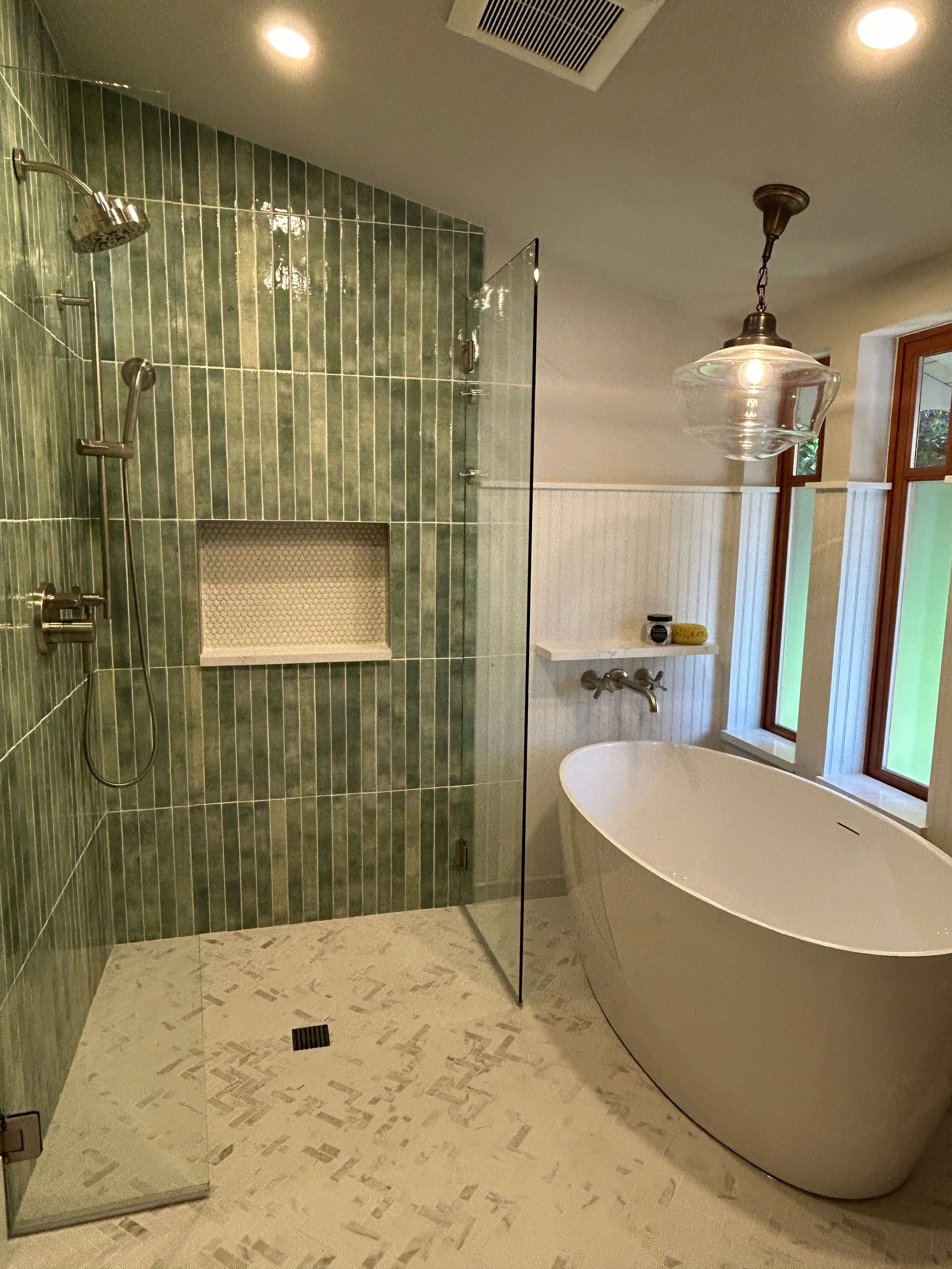 Modern bathroom with green tiled shower, glass partition, freestanding tub, and large windows
