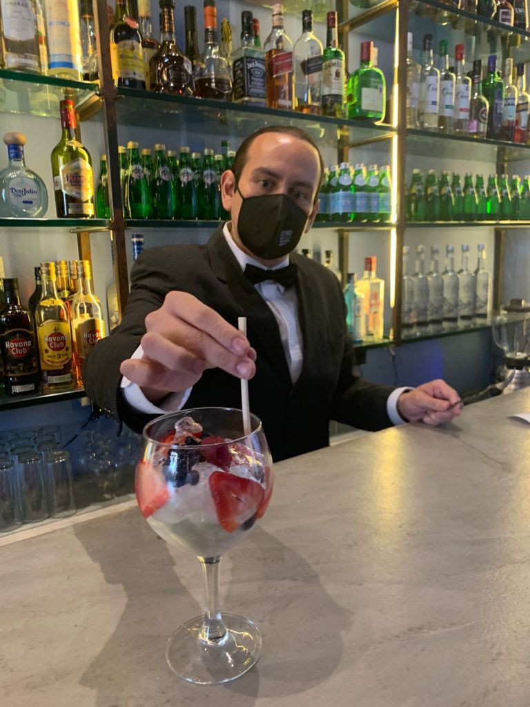 Un hombre con esmoquin sostiene una pajita en una copa de martini.