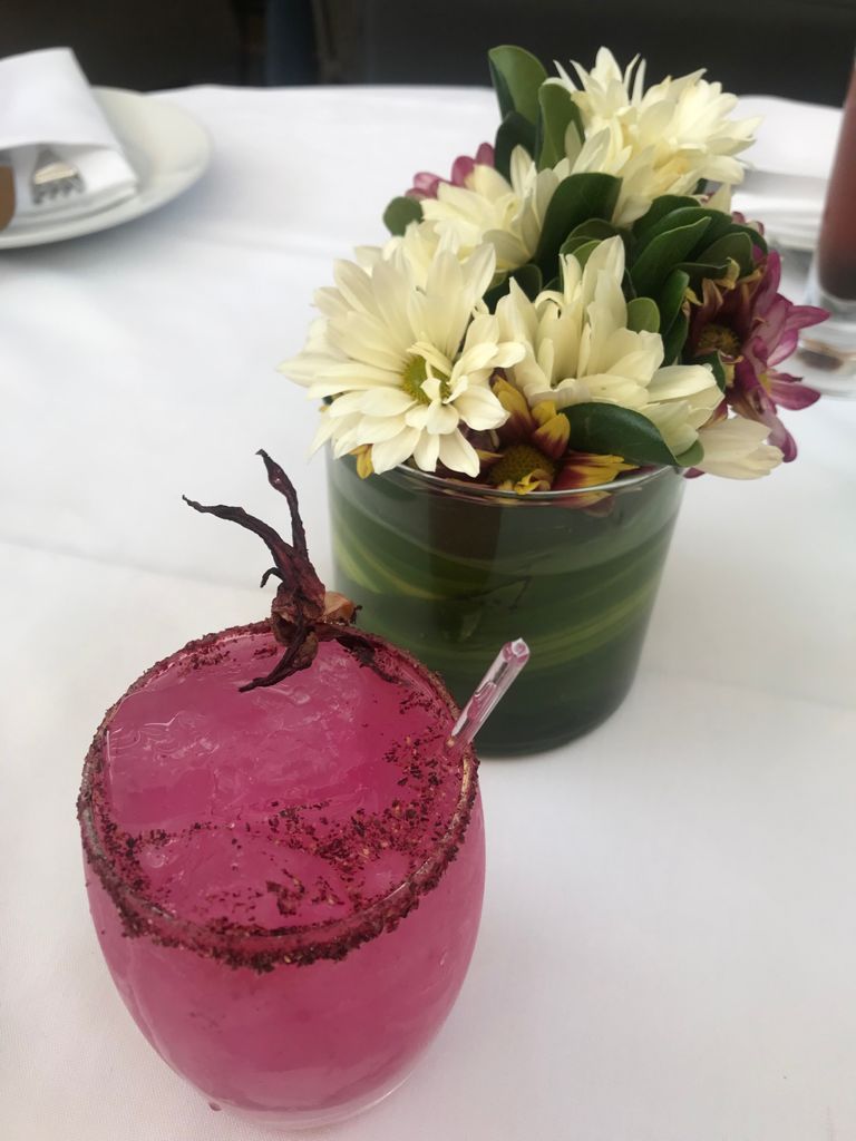 Una bebida rosa junto a un jarrón de flores sobre una mesa
