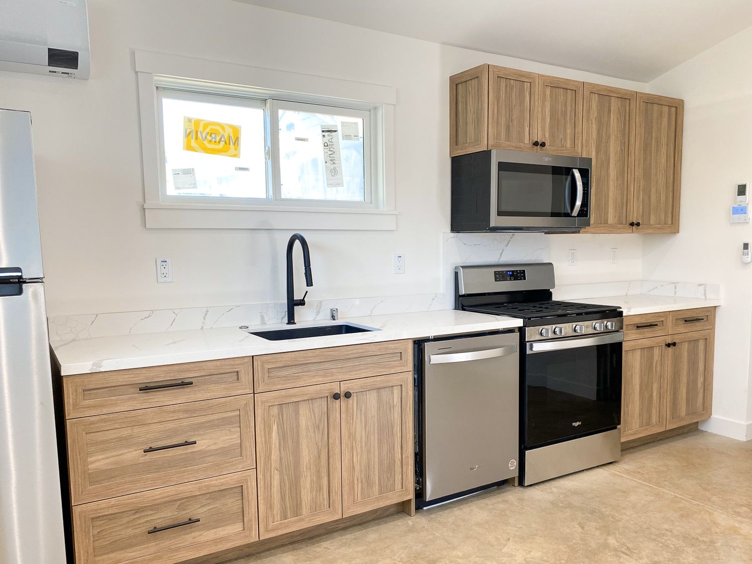 A modern kitchen with light wood cabinets, white countertops, and stainless steel appliances.