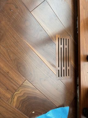Plancher en bois avec une grille d'aération décorative rectangulaire.