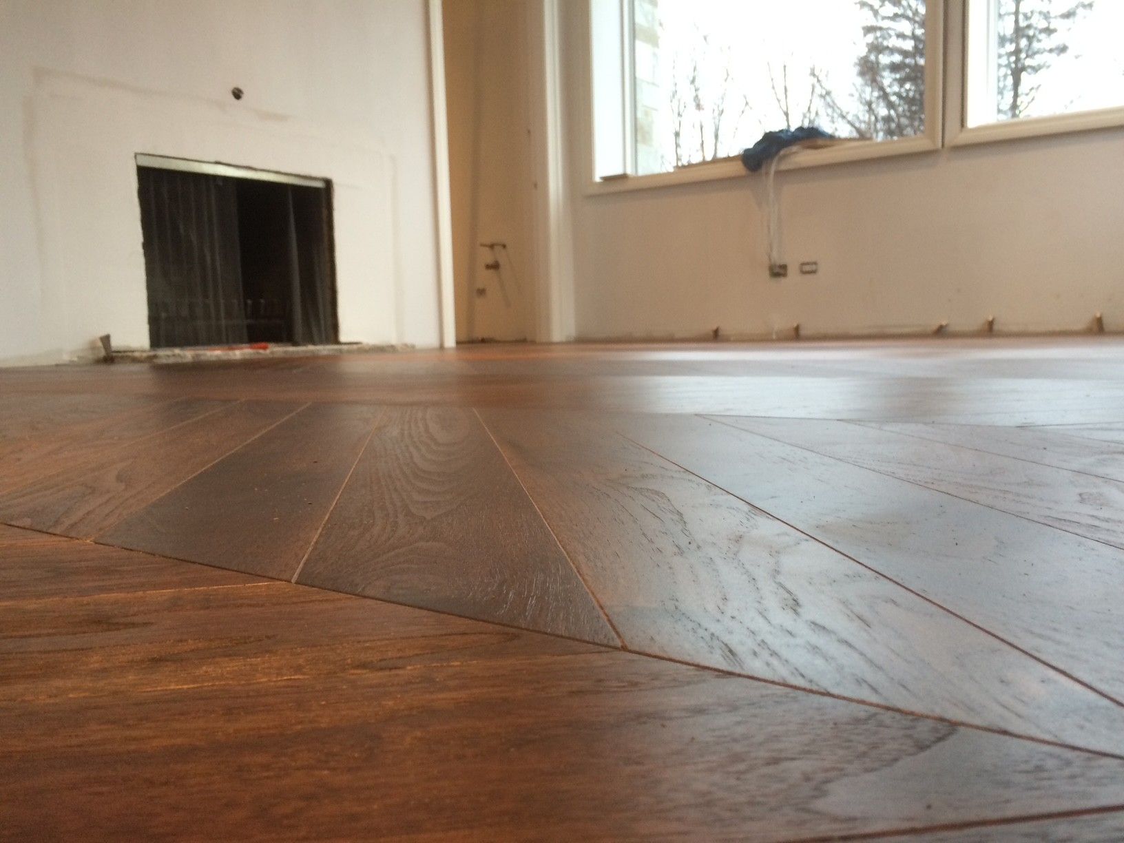 Pose d'un parquet foncé dans une pièce avec cheminée et grandes fenêtres.