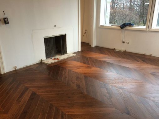Chambre avec parquet à chevrons, murs blancs, cheminée et fenêtre donnant sur l'extérieur.