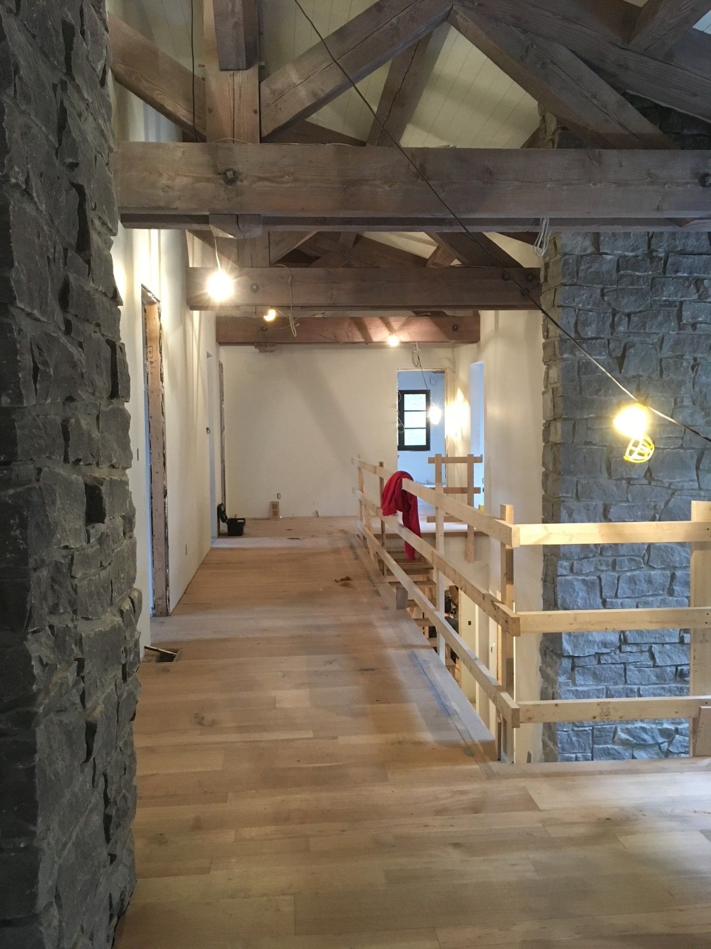 Intérieur d'une maison en construction, montrant des poutres en bois, des murs en pierre et un couloir avec un parquet.