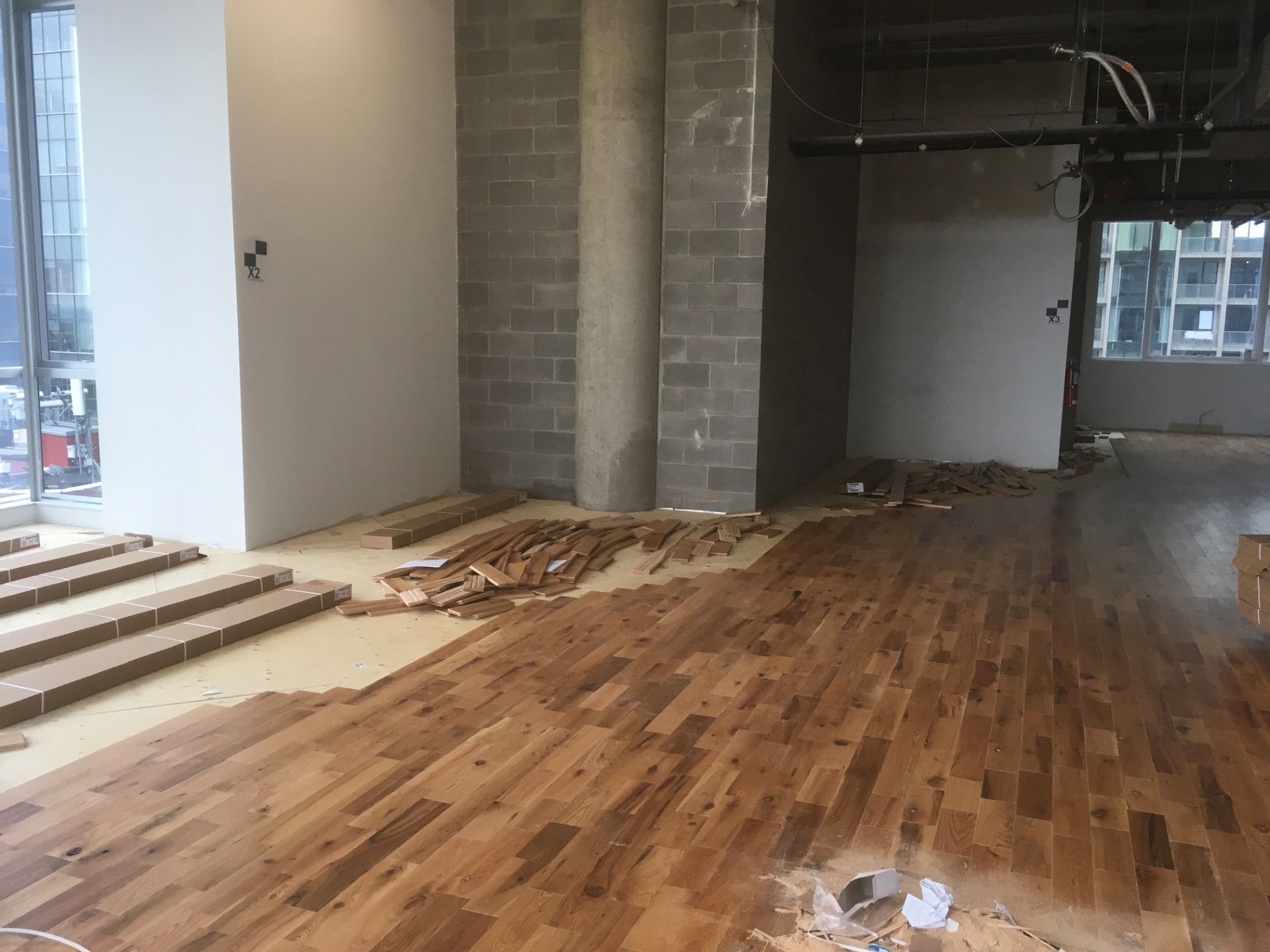 Intérieur en cours de rénovation, pose de parquet. Lames brunes posées sur une chape. Pilier et murs en parpaings gris.