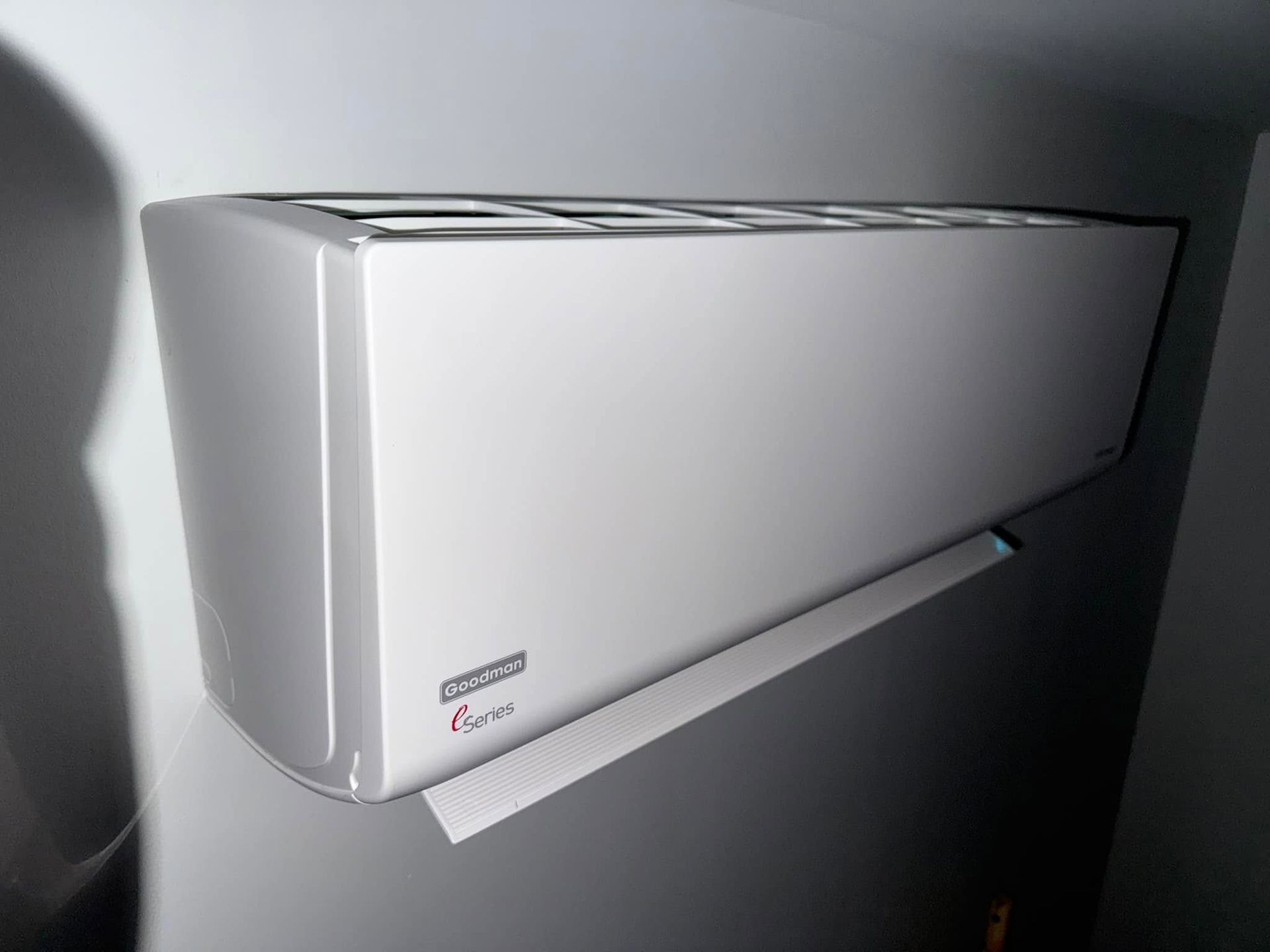White wall-mounted air conditioner on a gray wall, shown in side view.