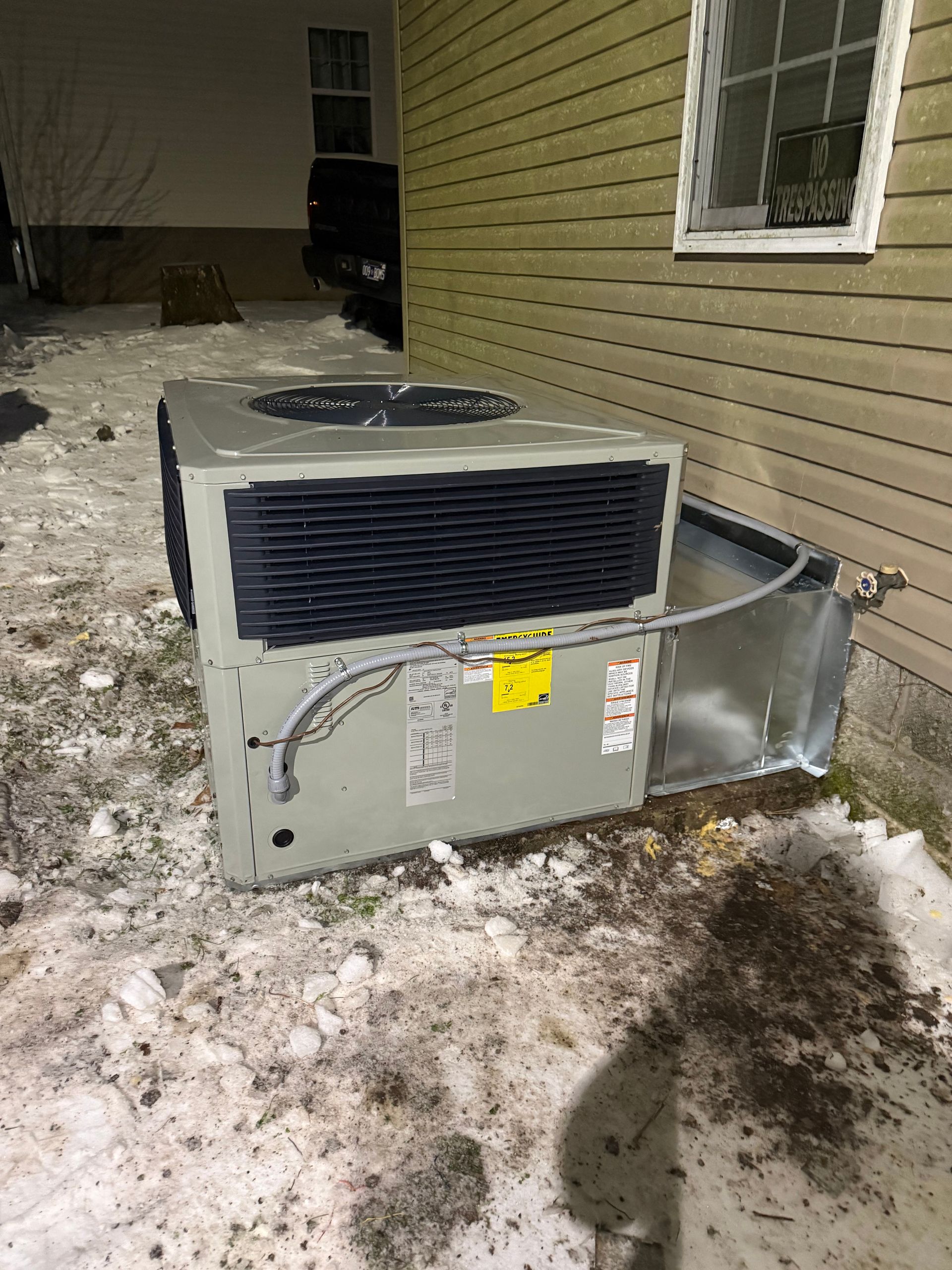 Outdoor HVAC unit beside a house, with bent metal panels and snow on the ground.