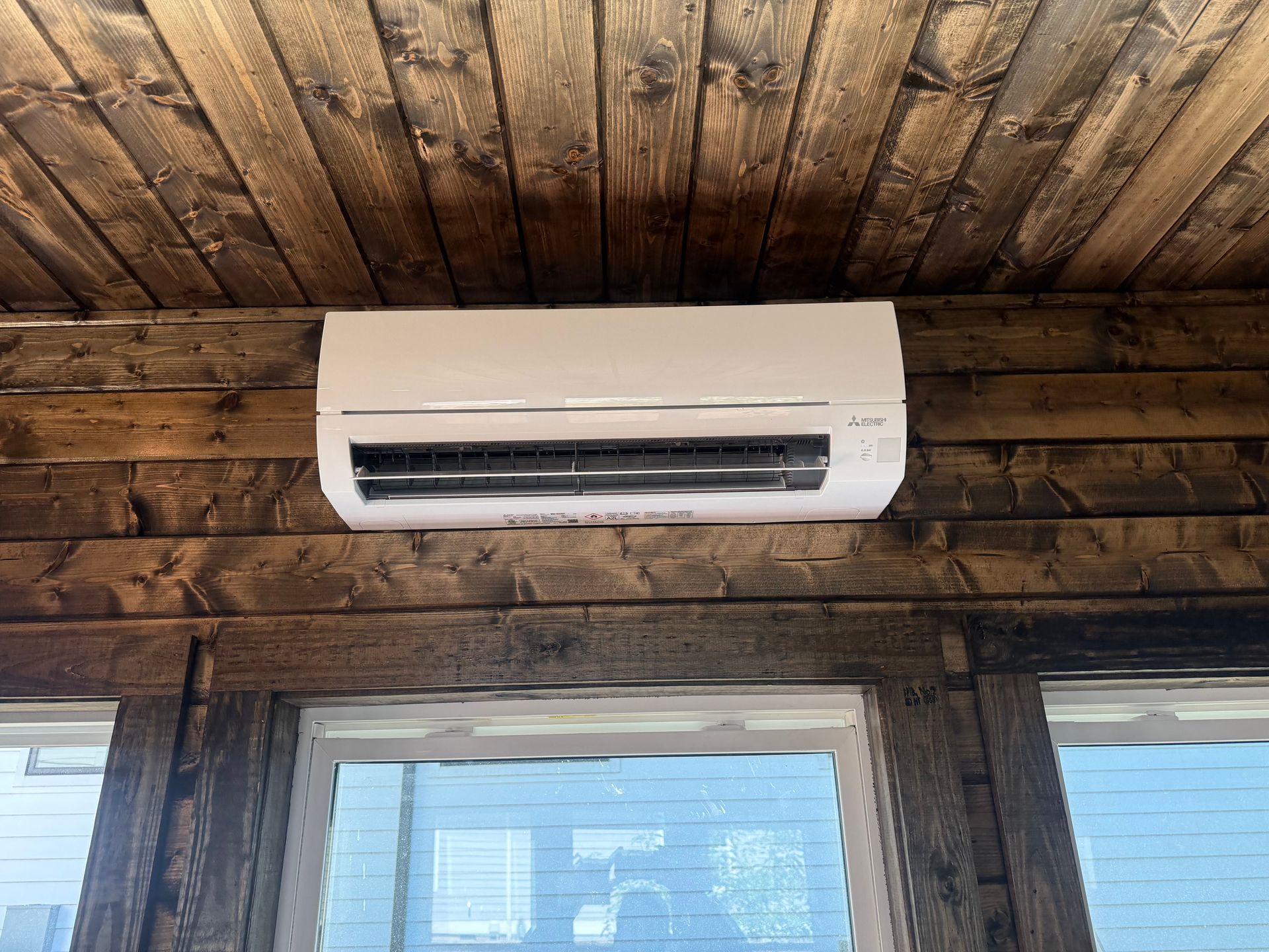 White wall-mounted air conditioner above a window on a rustic wooden wall and ceiling