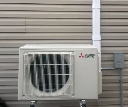 Outdoor Mitsubishi Electric AC unit mounted on a beige exterior wall beside utility conduit